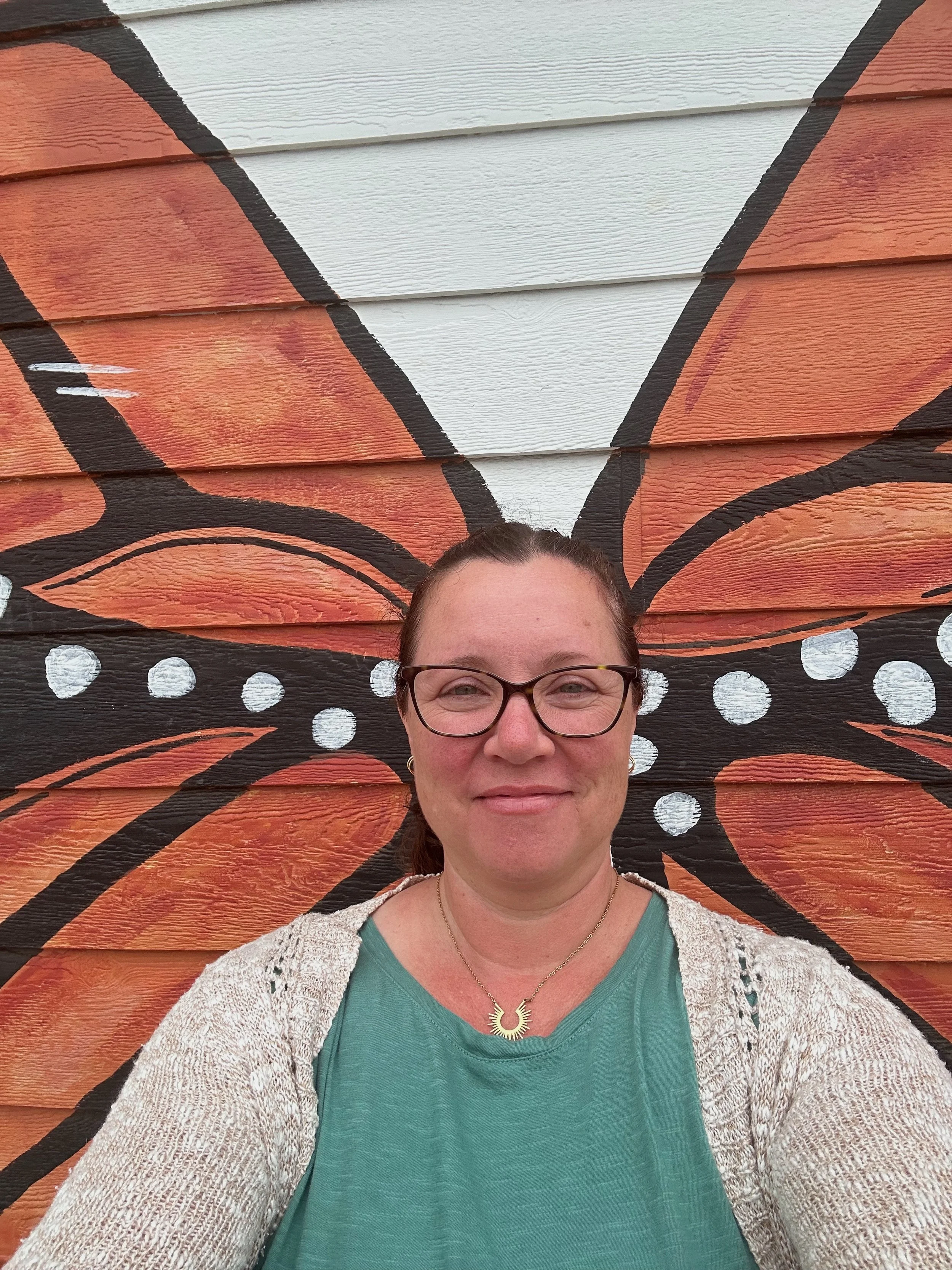 Eileen Zimmerman, life purpose coach, smiling in front of a monarch mural