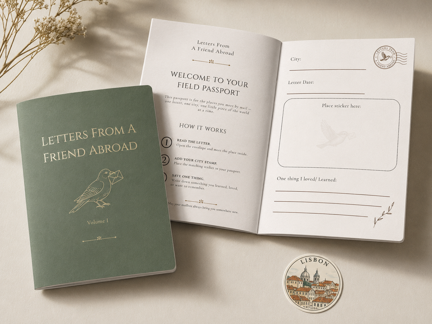 A green journal titled "Letters From A Friend Abroad" with a bird illustration on the cover, placed next to an open booklet titled "Welcome to Your Field Passport" with instructions on how to use it, a sticker of a bird, and a round sticker of Lisbon cityscape, all on a light-colored surface with dried flowers in the background.