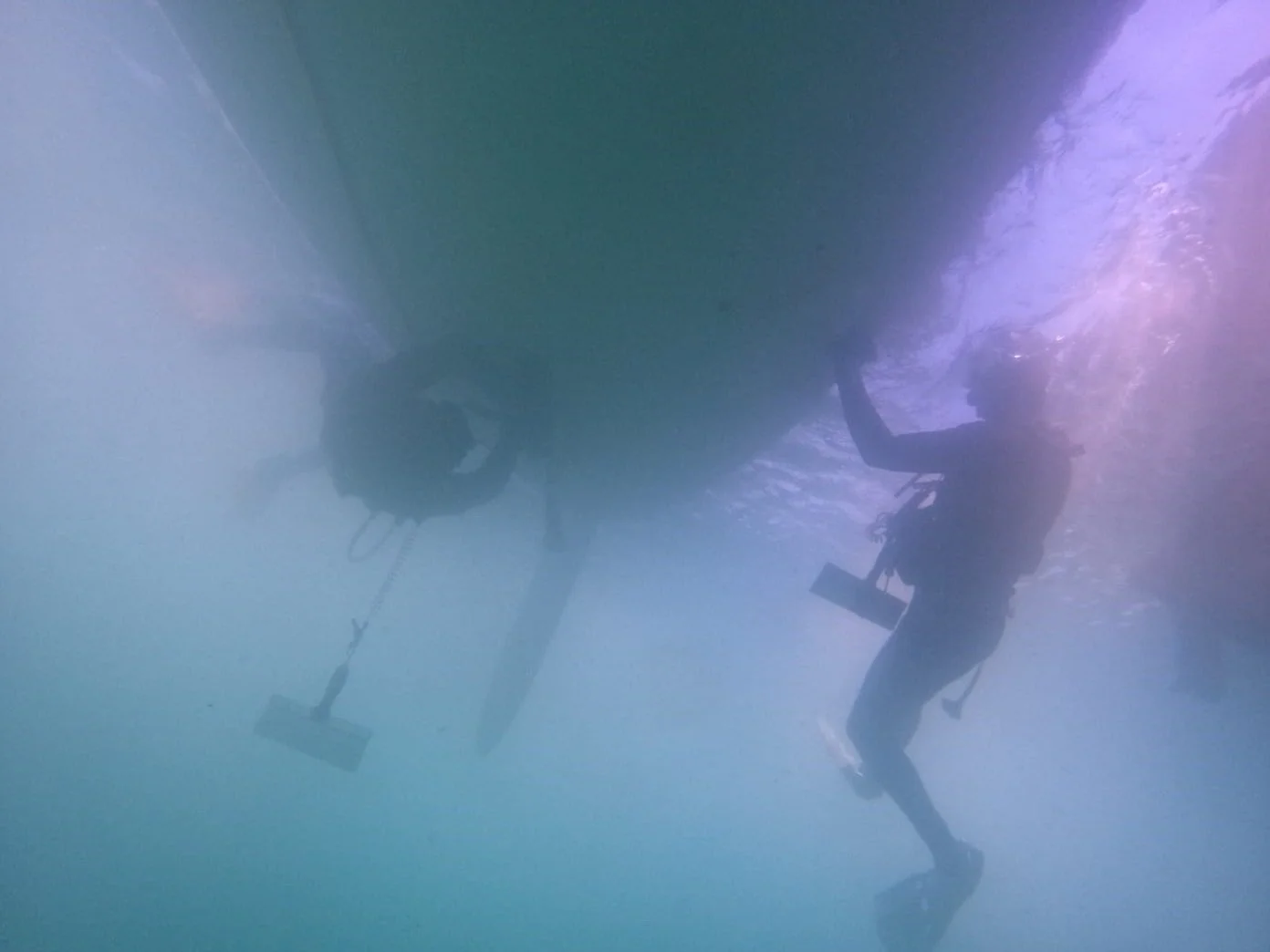 Two scuba divers underwater conducting vessel maintenance and cleaning activities