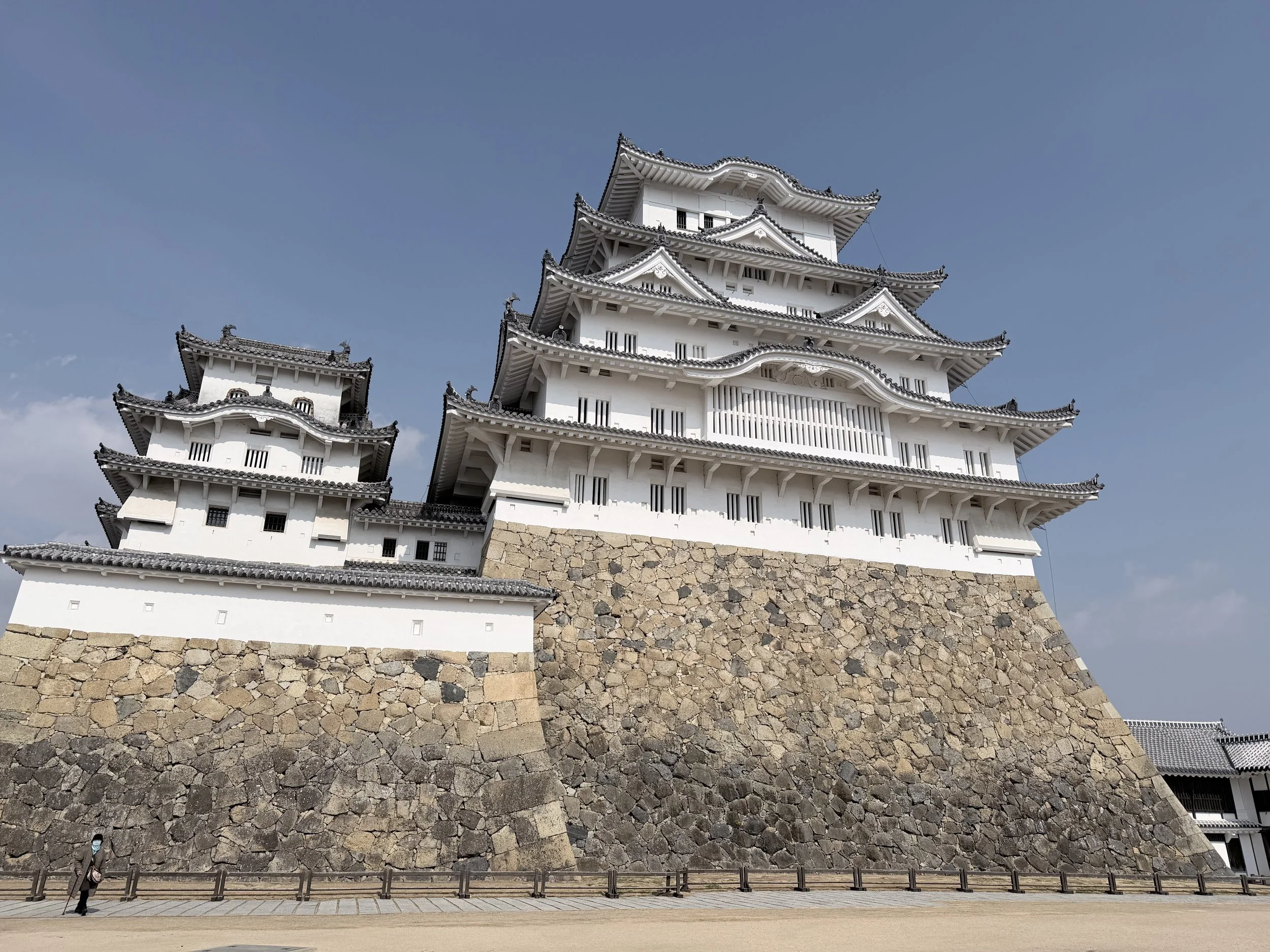 Traditional Japanese castle with white walls and tiered, curved roofs, built on a stone foundation, against a clear blue sky.
