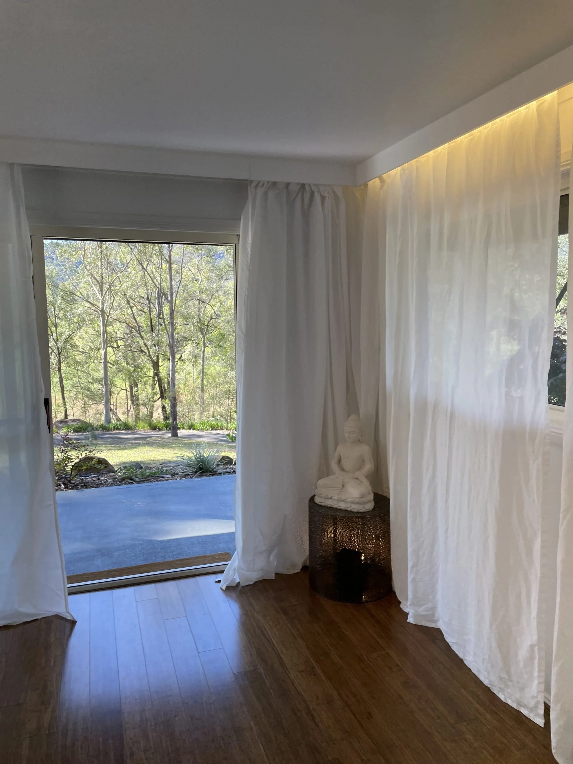 Open door leading outside to a natural landscape with trees, and a white Buddha statue on a side table inside.
