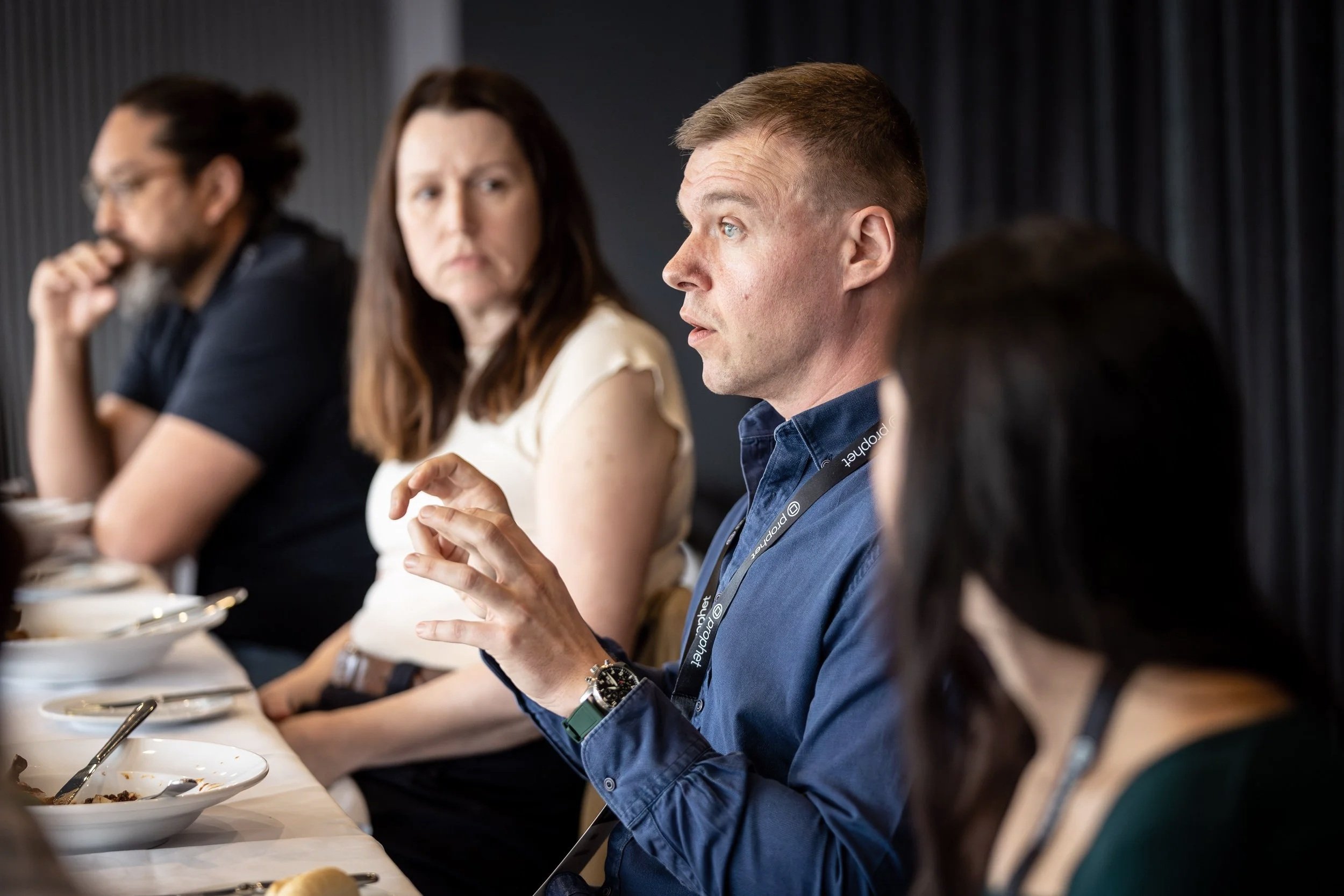 People sitting at a long table during a business meeting or conference, engaged in conversation and eating.