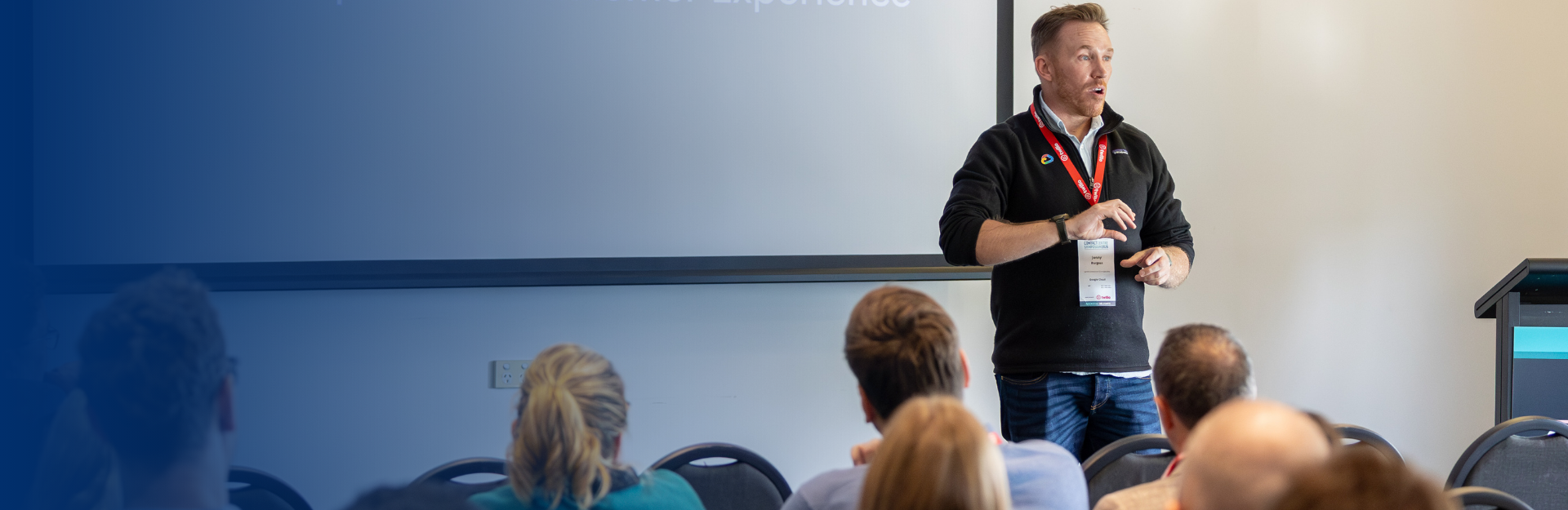 A man giving a presentation to a group of people at a conference, standing in front of a projection screen.