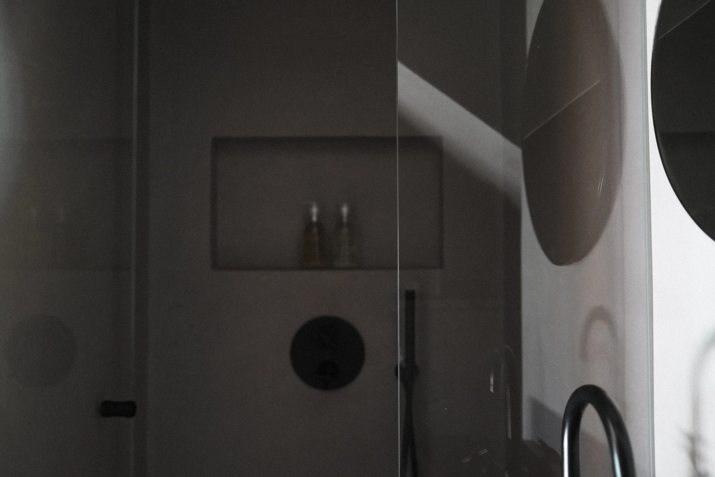 Close-up of a washing machine door, showing the dark interior with a bottle of detergent inside, viewed from the side.