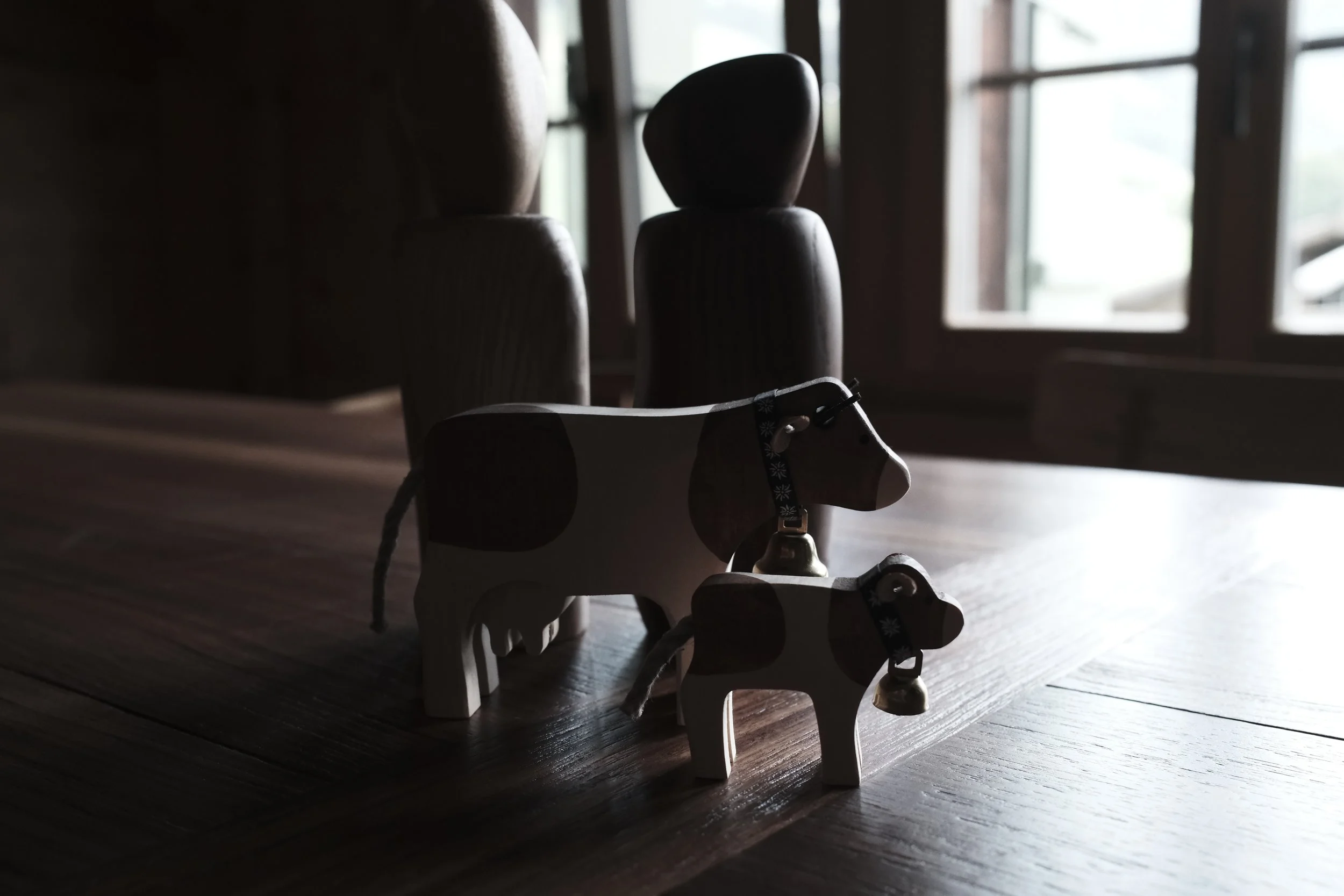 Small wooden horse toy with a black collar, placed on a dark wooden floor near a window with natural light.
