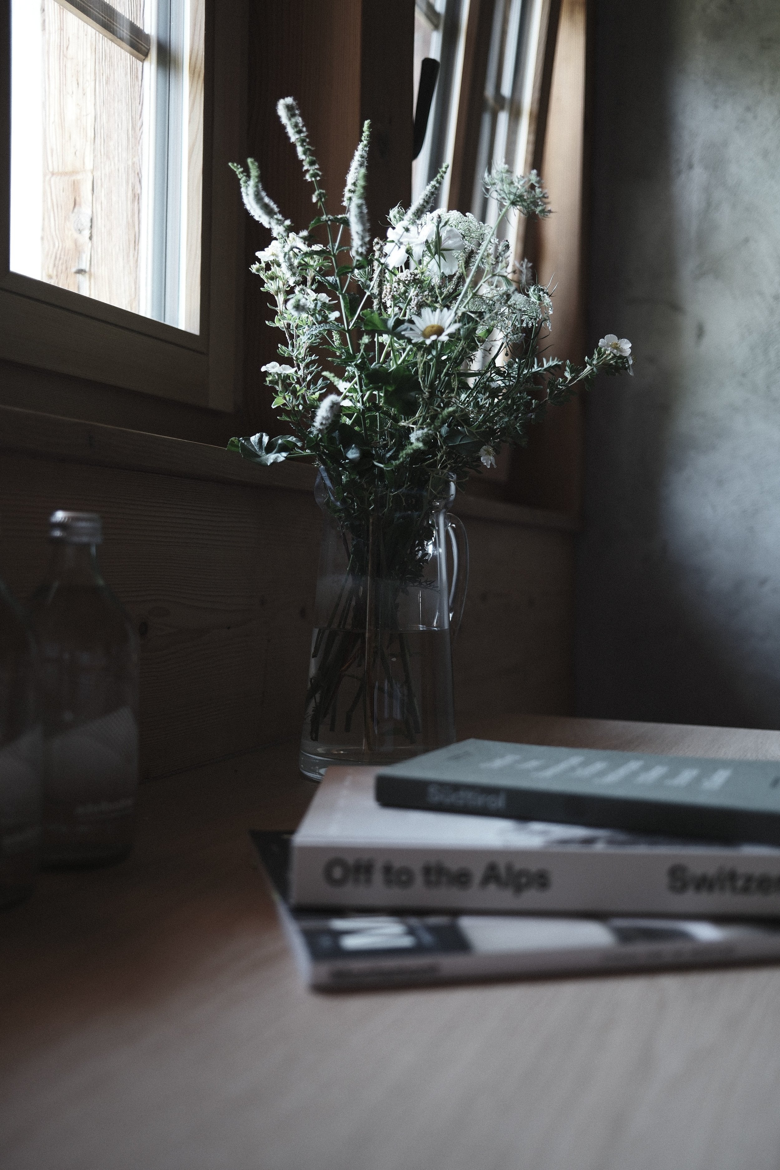 A bouquet of white and green flowers in a glass vase on a windowsill, viewed in low light.