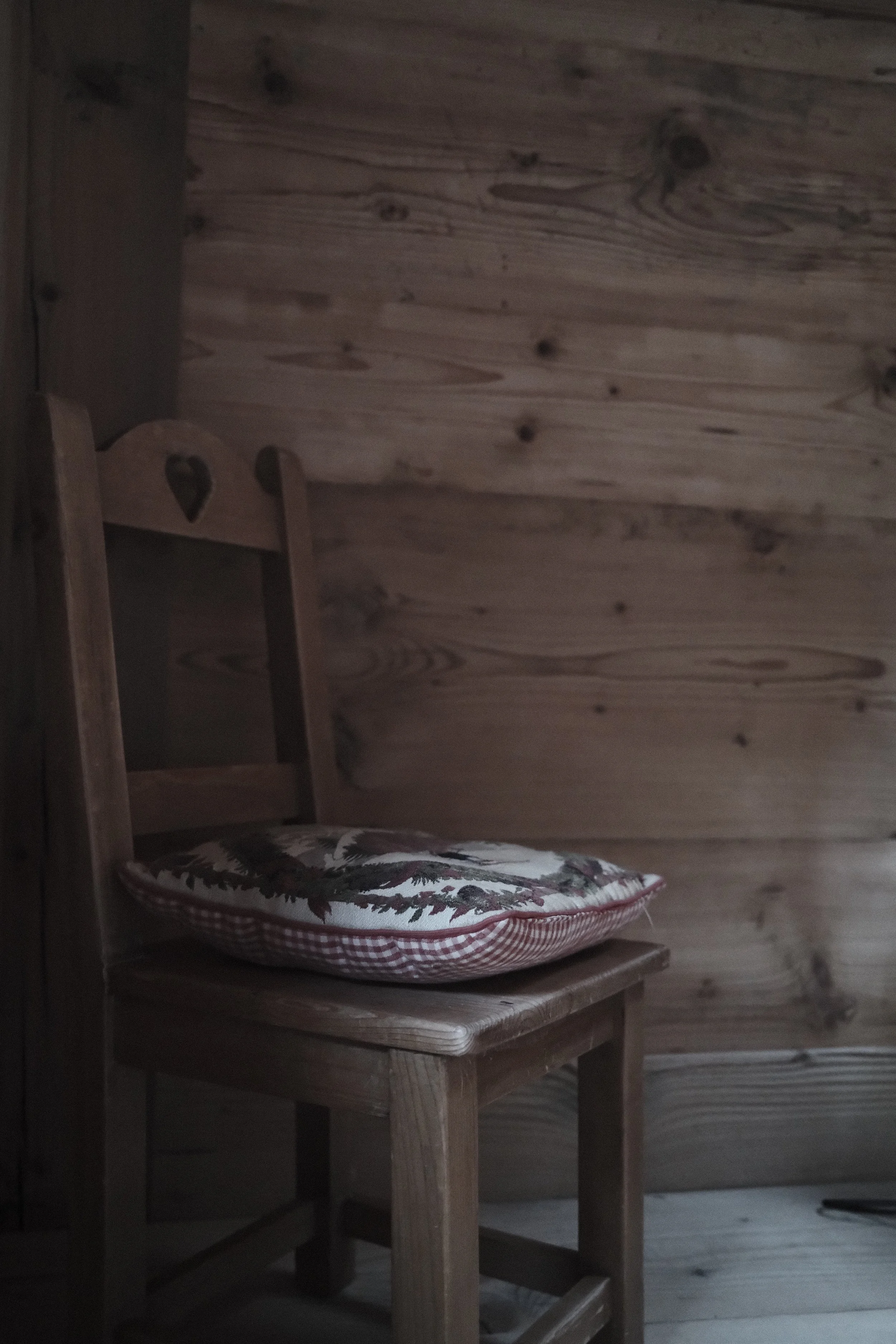 A wooden chair with a patterned cushion on it, placed next to a wooden wall in a rustic room.