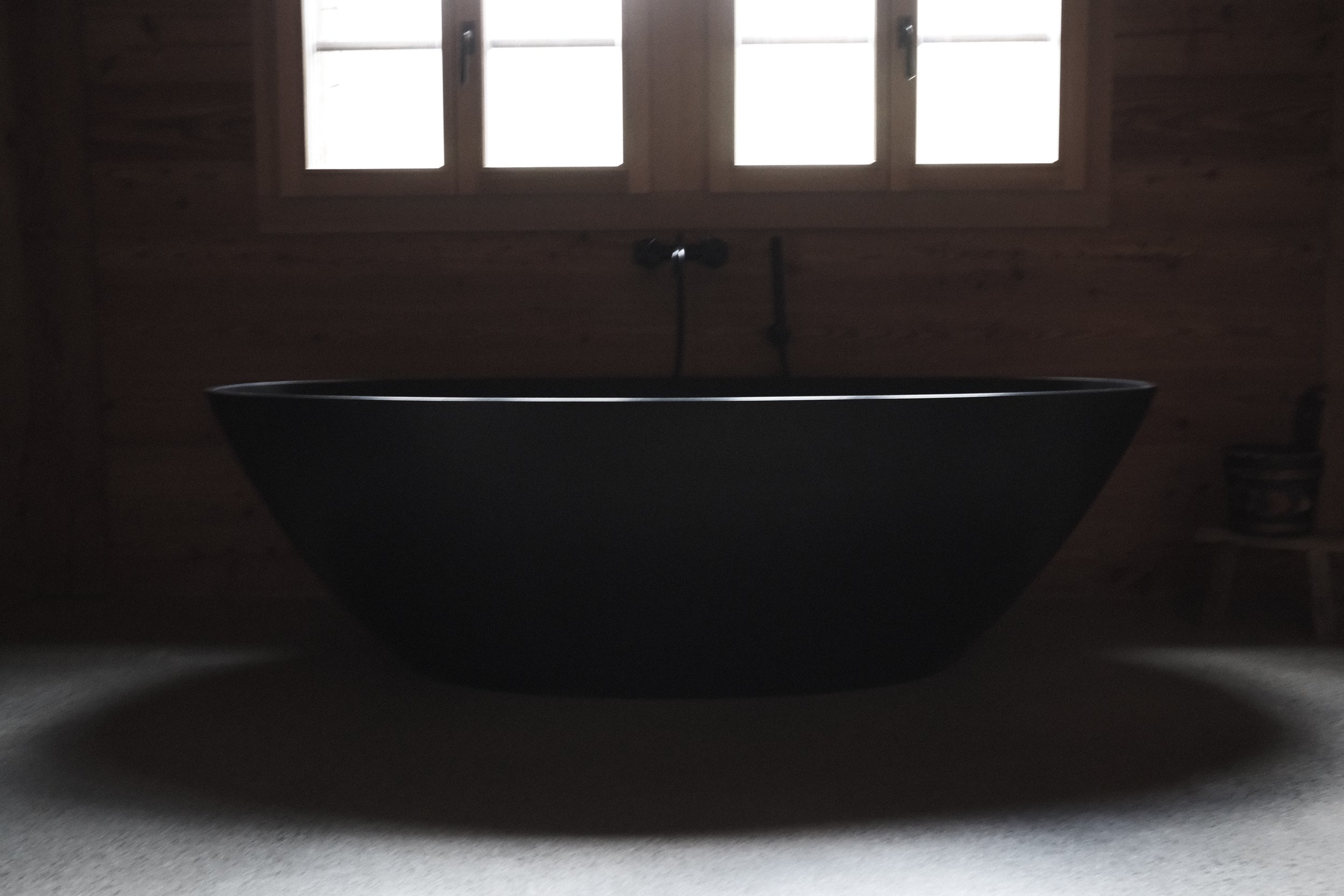 A black bathtub situated in a dimly lit room with wooden walls and a window letting in natural light.