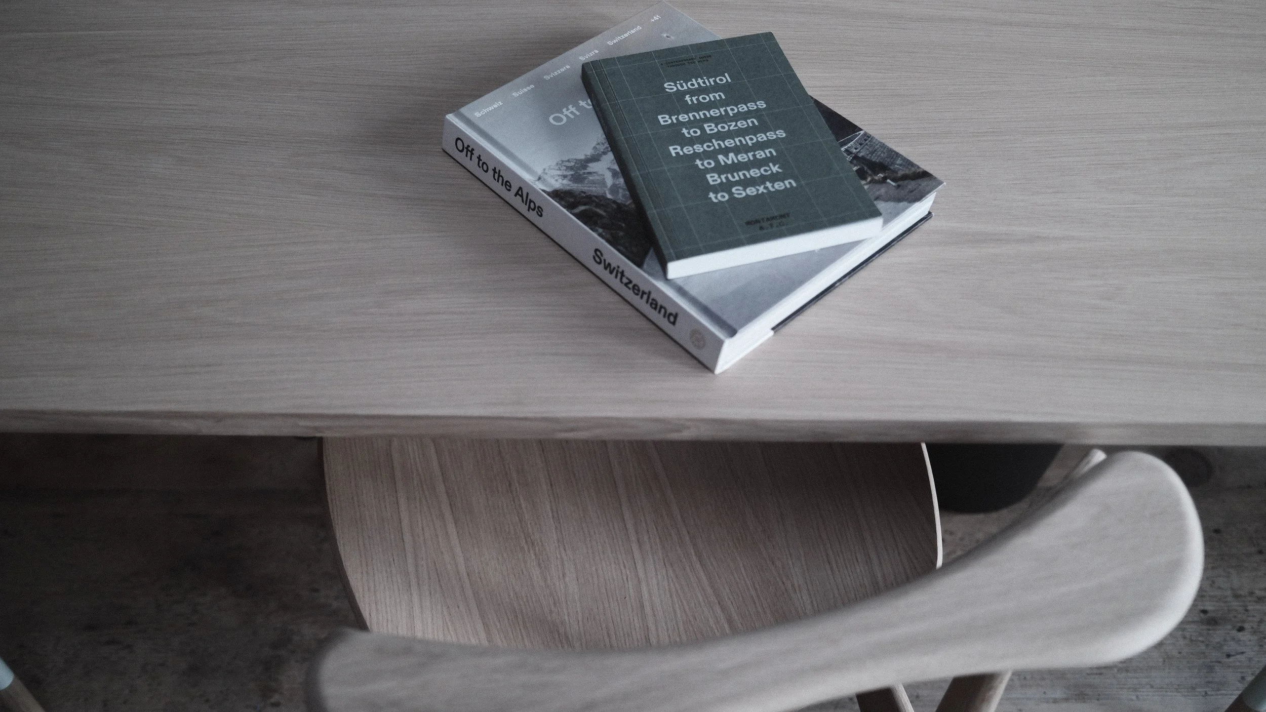 Two books stacked on a light-colored wooden table, one titled 'Off to the Alps' and the other about Südtirol from Brennerpass to Bozen.
