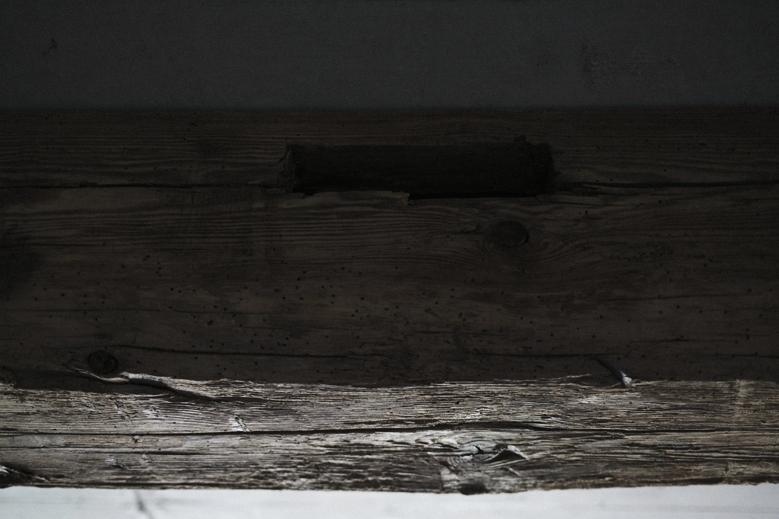 Close-up of a wooden surface with visible grains and knots, blackened from age or weathering.