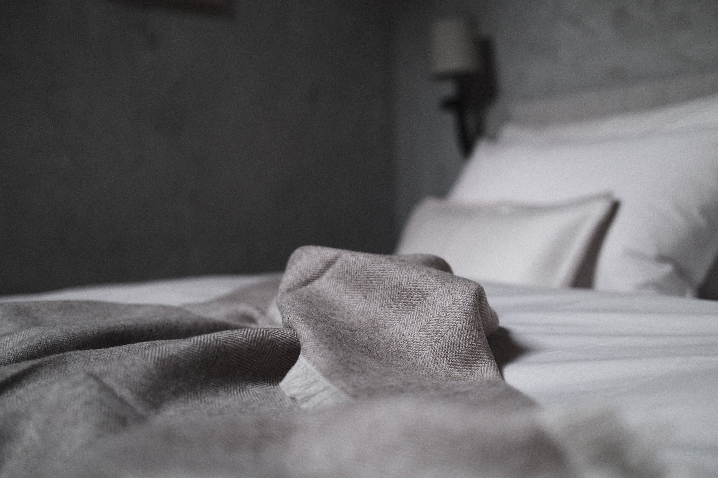 Close-up of a bed with gray and white patterned blankets and pillows, a person lying down, and a nightstand with a lamp in modern, minimalistic bedroom.
