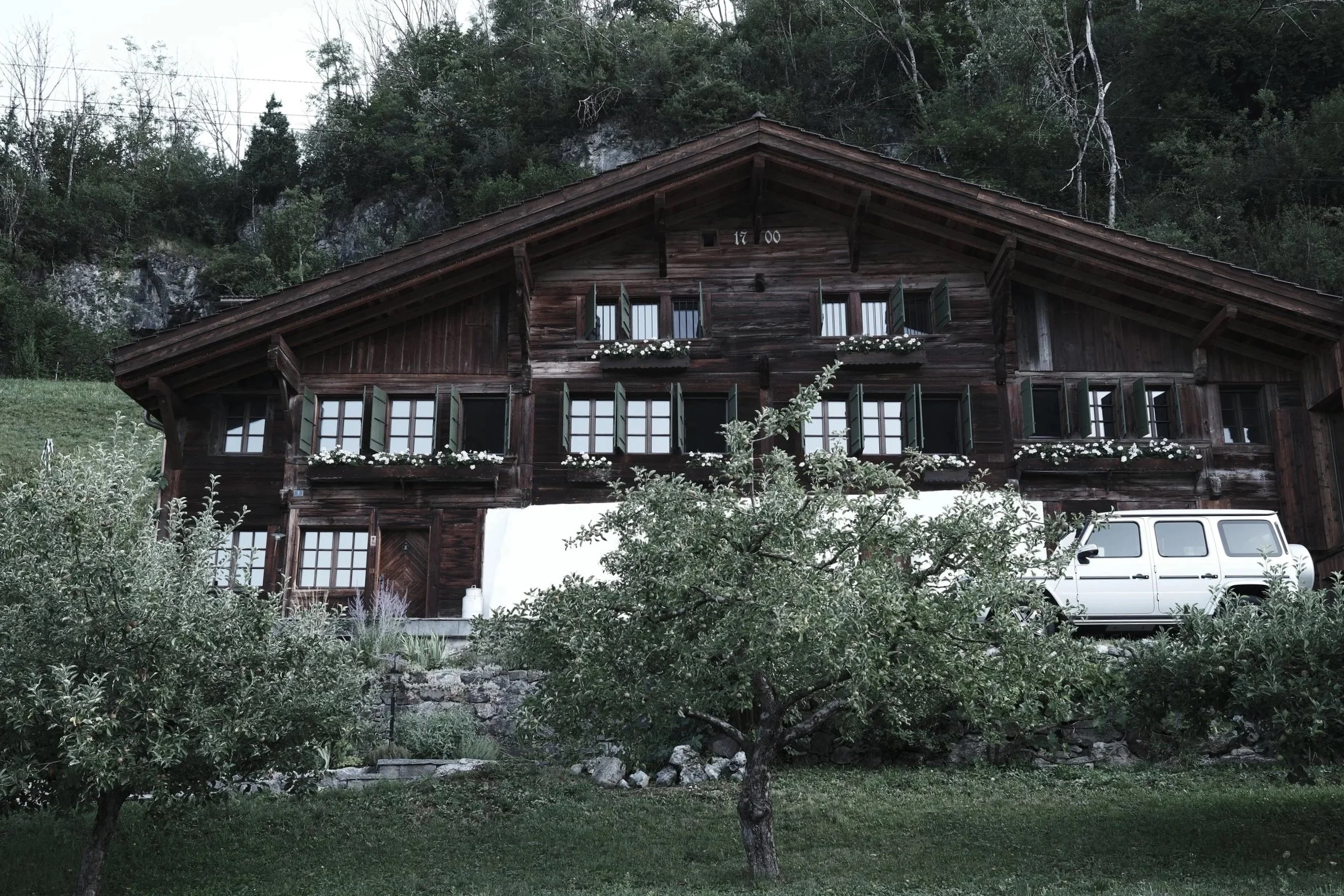 Front façade of Haus Mannenberg, a restored 18th-century Swiss chalet in Mannried near Gstaad, surrounded by orchards and the Bernese Oberland mountains.