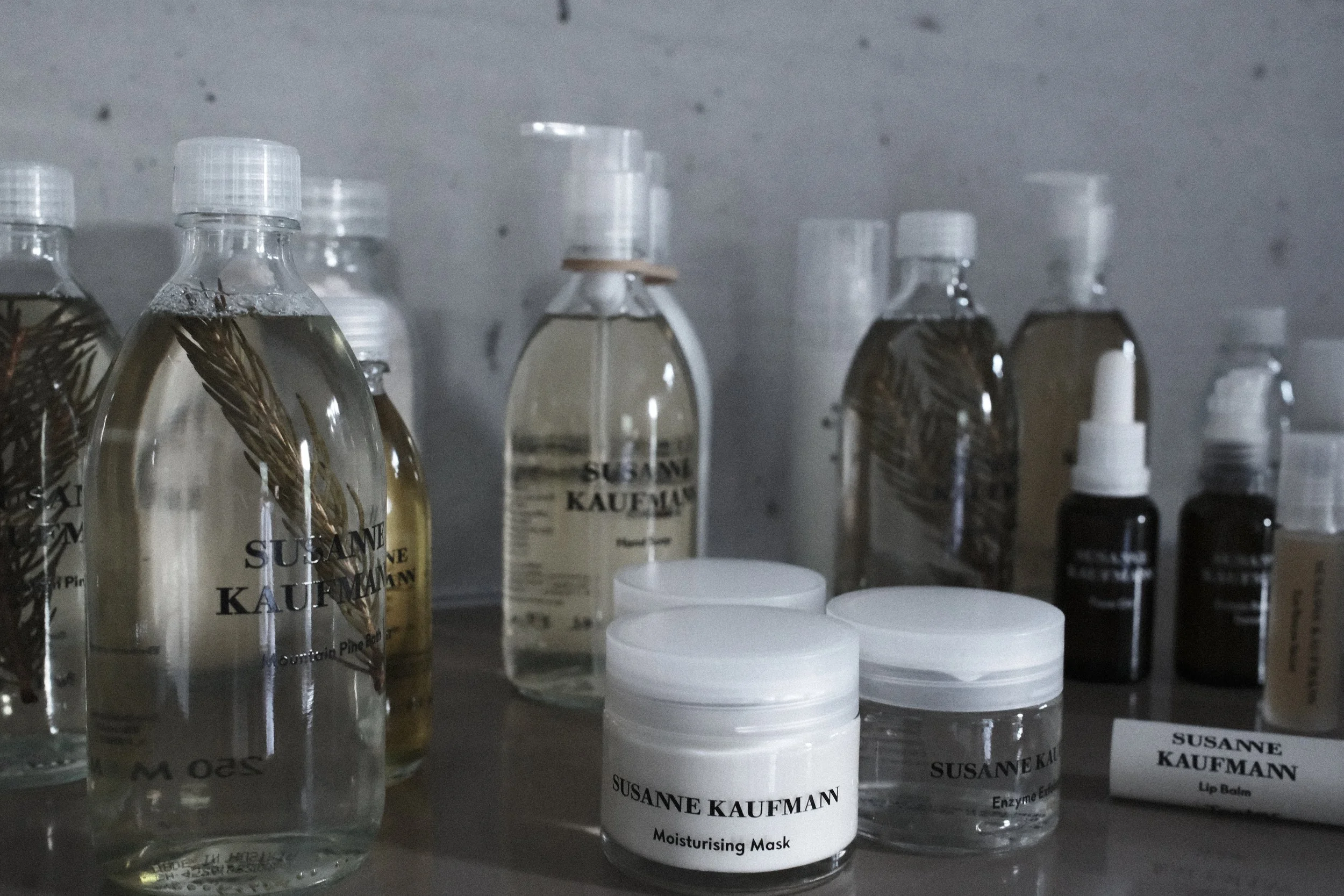 Several bottles and containers of skincare products labeled with 'Susanne Kaufmann' on a shelf, including moisturizing masks, lip balms, and enzyme eye creams.
