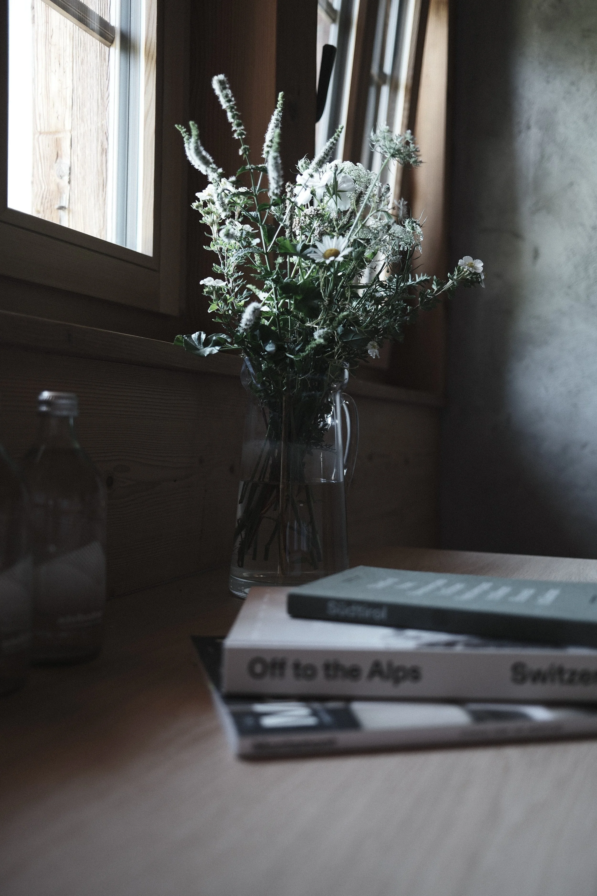 A bouquet of white flowers in a glass vase sitting on a windowsill with sunlight coming through the window.