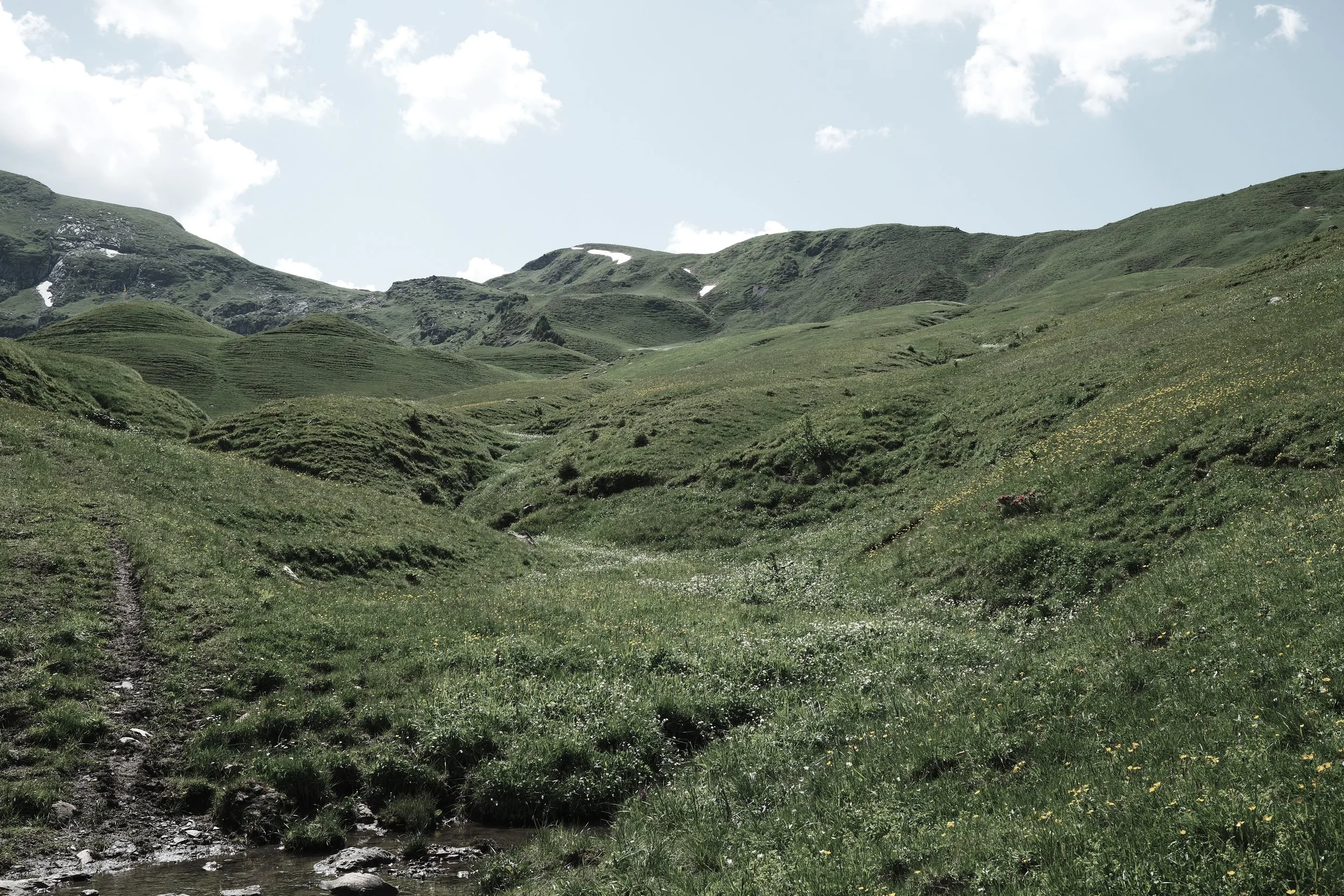 Green rolling hills and mountain landscape under blue sky with scattered clouds.