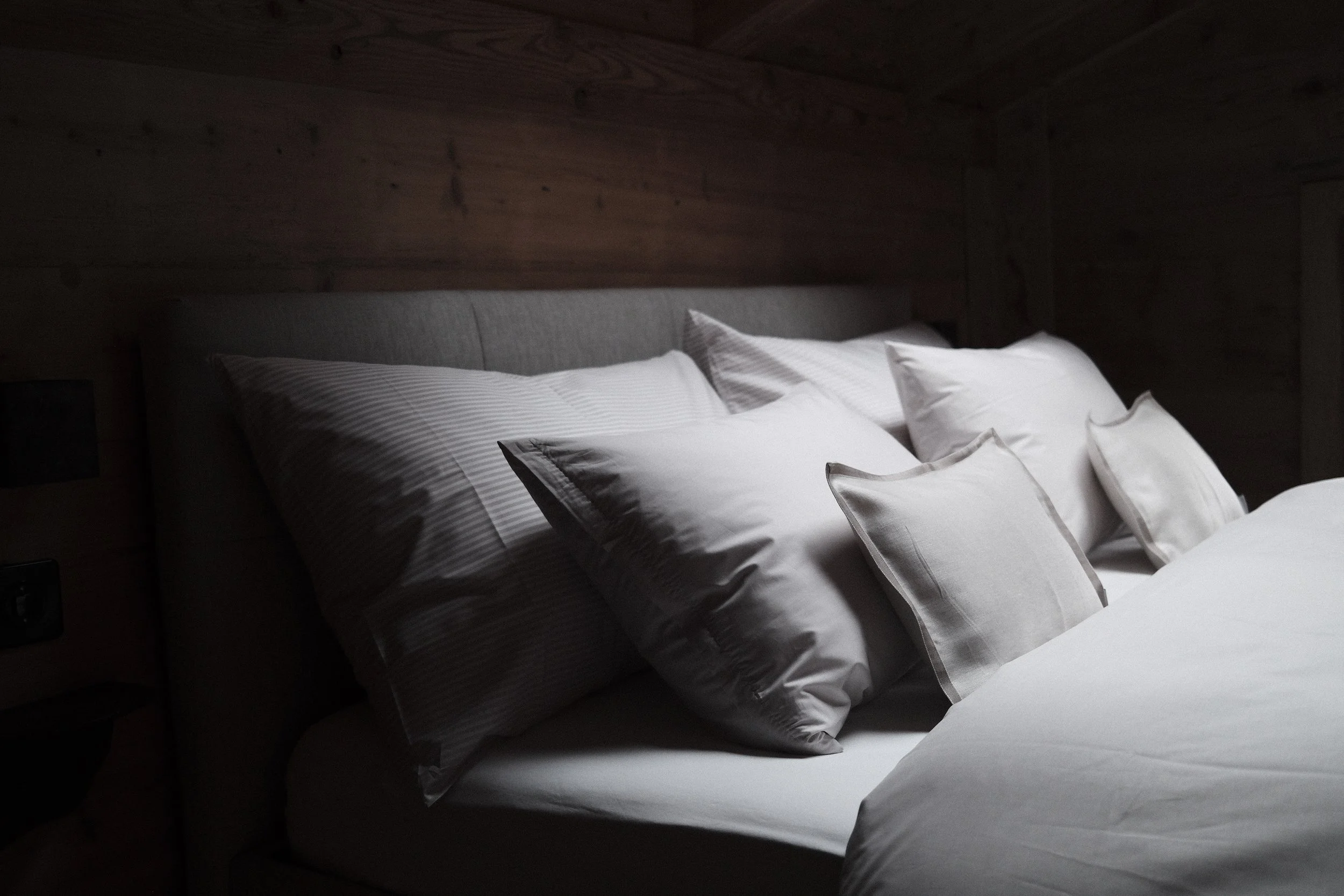 A bed with multiple white and striped pillows in a room with wooden walls.