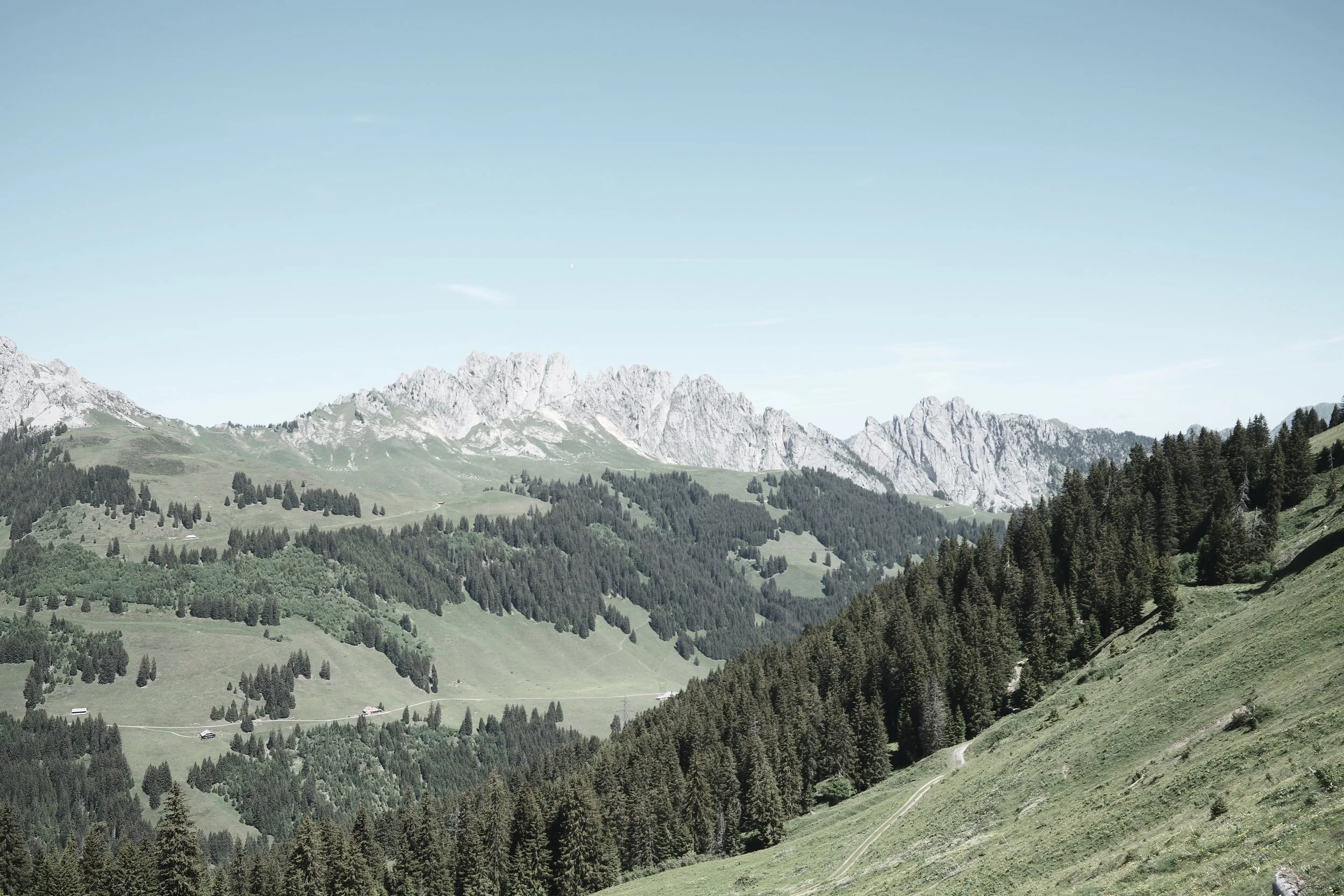 Scenic view of mountains with rocky peaks, green hills, and forests under a clear blue sky.