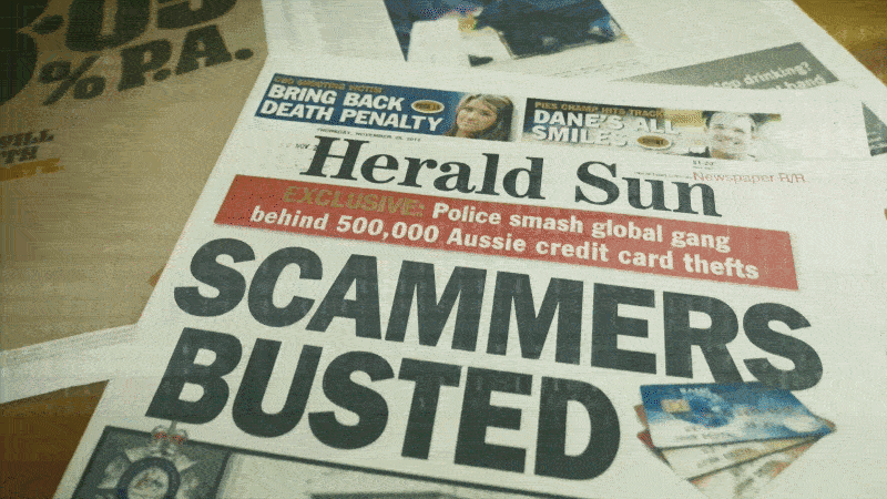 A newspaper page with large headline text reading "SCAMMERS BUSTED" and a smaller red banner stating "Exclusive police smash global gang behind 500,000 Aussie credit card thefts." There are also smaller headlines at the top about the death penalty, a smile, and other news stories, along with some credit cards placed on the page.
