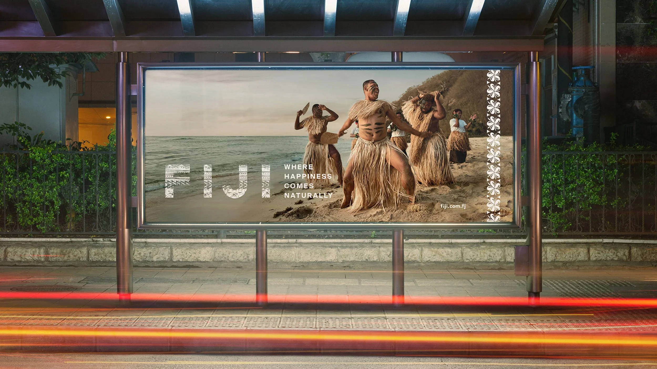 An advertisement showing traditional dancers in grass skirts on a beach, with the text 'WHERE HAPPINESS COMES NATURALLY' and the URL 'fiji.com.fj'.
