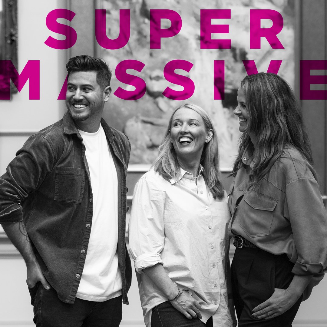 Three people, two women and one man, smiling and talking in a casual setting. Black and white photo with the words 'Super Massive' in bold pink letters over the image.