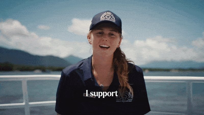 A woman in a navy blue uniform and cap smiling on a boat with a mountain and lake background, with the subtitle 'I support' visible.