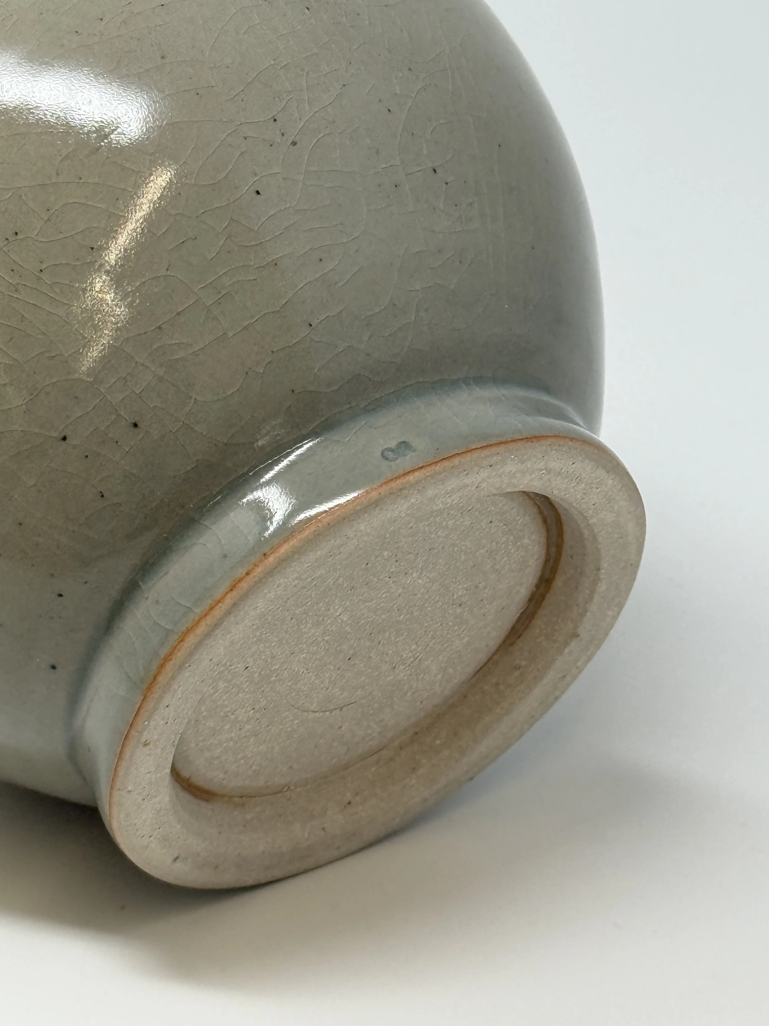 Close-up image of the bottom of a ceramic mug, showing uneven glaze and a small glaze bubble or imperfection.