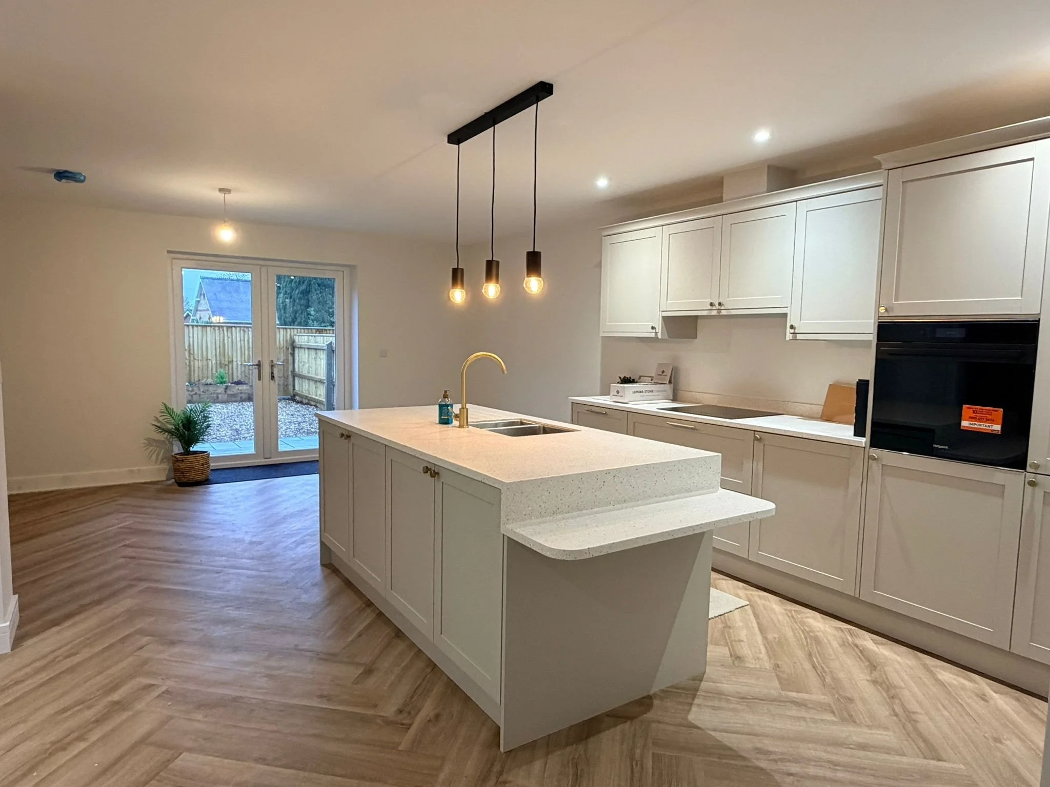 Modern kitchen with white cabinets, an island with a light-colored countertop, and pendant lighting. A door leads to a backyard visible outside.