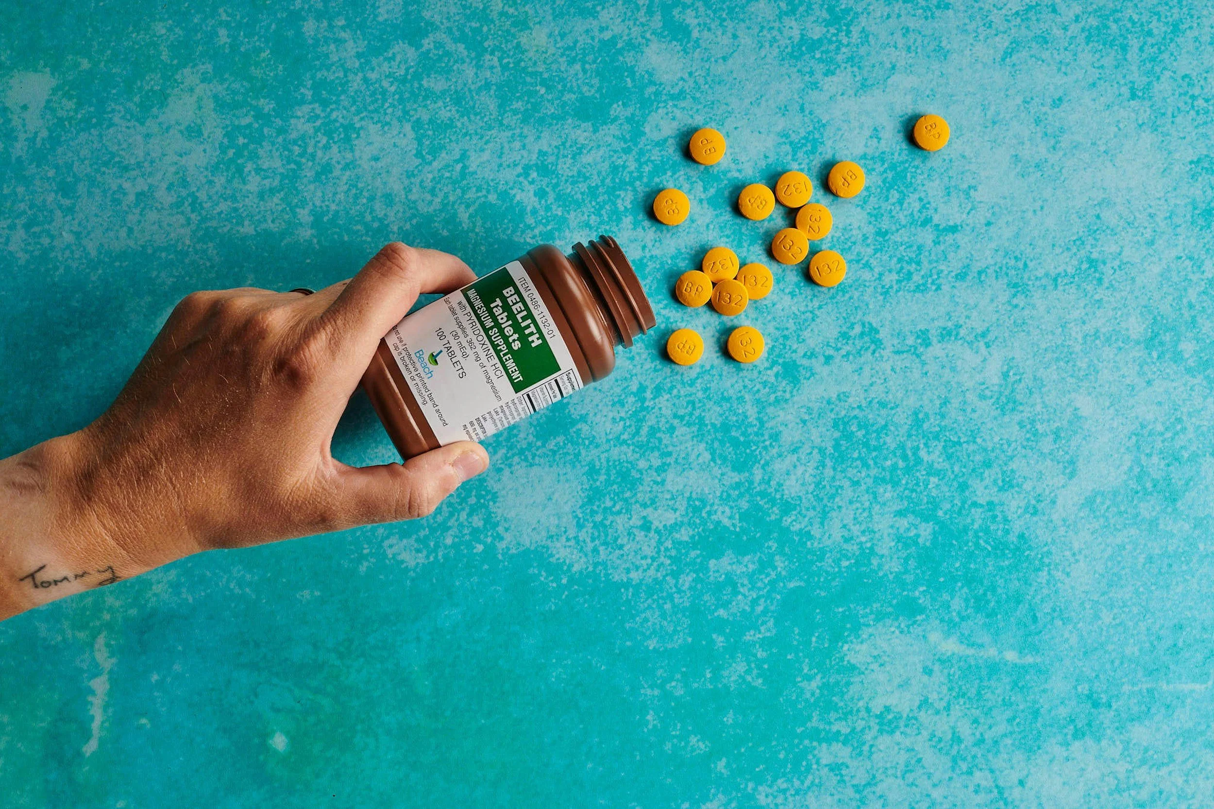 A hand holding a bottle of Bowel Health Tablets with yellow pills spilled onto a blue background.