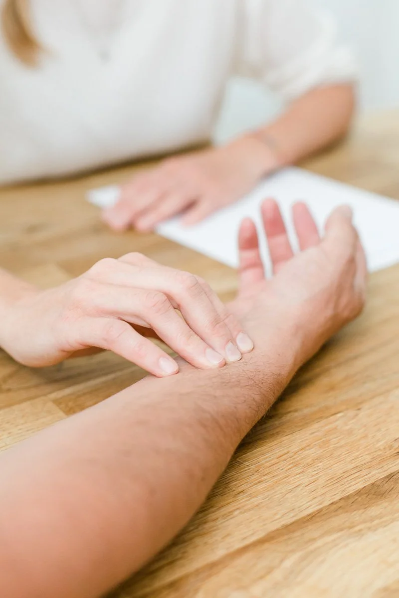 Jemand hält eine andere Person am Handgelenk und scheint dabei Akupressur oder Massage an einem eigenen Handgelenk durchzuführen.