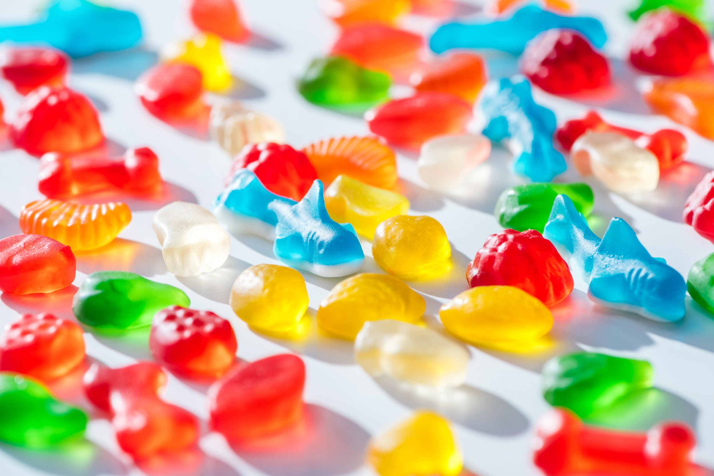 Colorful gummy candies scattered on a white surface with shadows.
