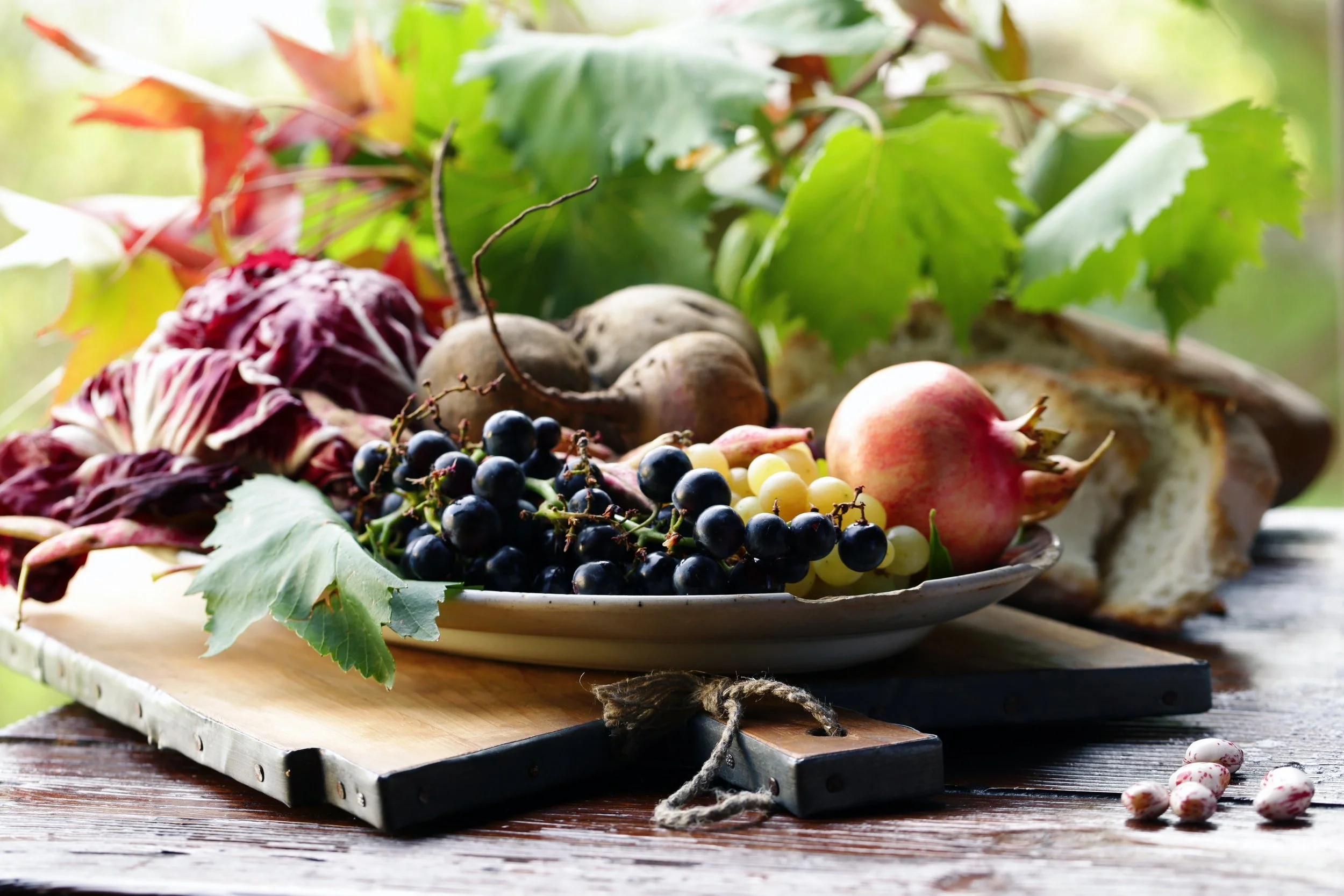 A plate of grapes, apples, and radicchio on a rustic wooden table with green leaves in the background.