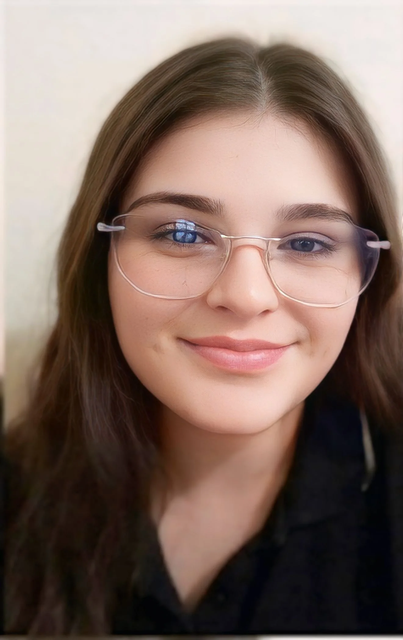 Close-up of a young woman with brown hair wearing glasses and a dark top, smiling softly.