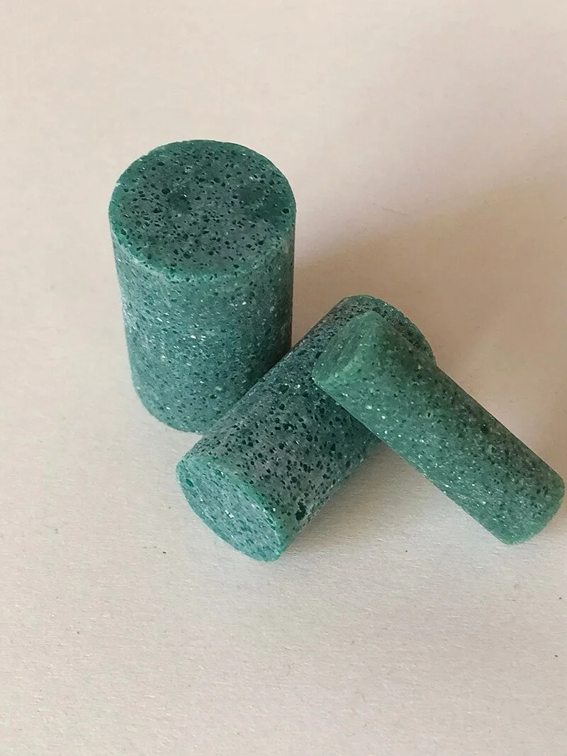 Drei grüne Tabletten auf einer weißen Oberfläche, eine steht aufrecht, zwei liegen flach