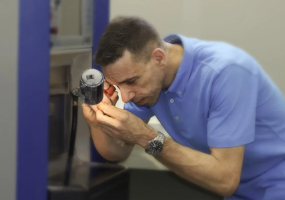 Mann in blauer Arbeitskleidung schaut durch ein Mikroskop.