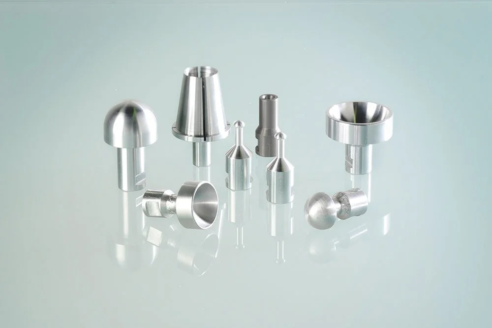Verschiedene metallische Werkzeuge und Werkstückteile auf einer glatten Oberfläche, wahrscheinlich in einem technischen oder industriellen Umfeld.