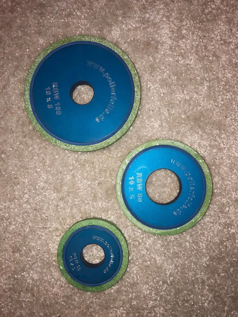 Drei runde Schleifscheiben mit blauen Oberflächen und grünen Rändern auf einem Teppichboden.