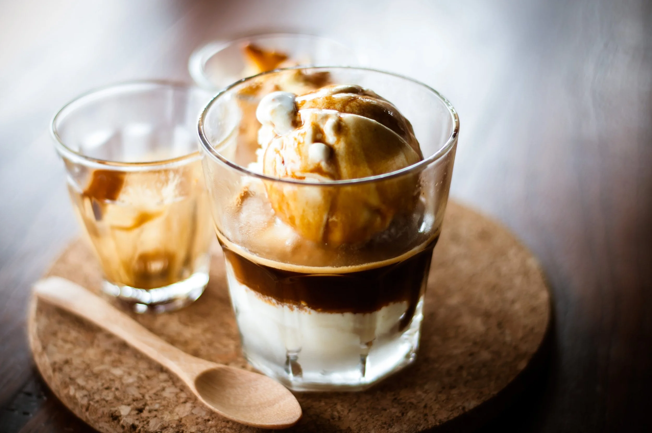 Ice cream with caramel and whipped cream in a glass, served with caramel drizzle, on a wooden tray with a spoon.