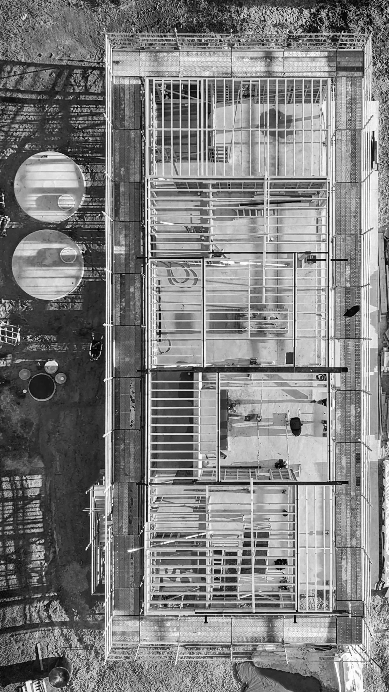 Black and white photo of a multi-story building under construction with exposed framing, scaffolding, and construction materials on the ground.