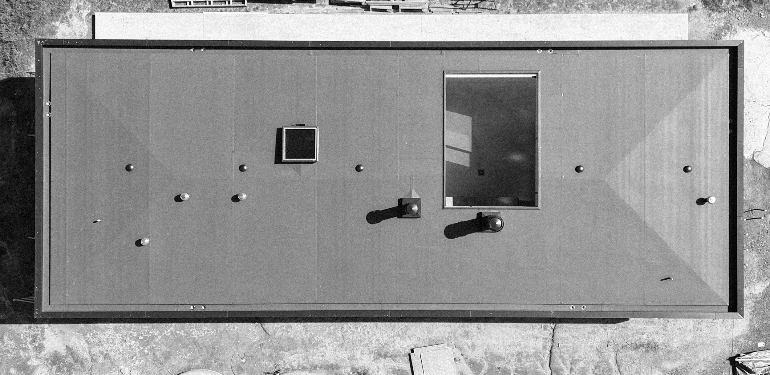 An aerial view of a flat rooftop with various vents, a small window, and a large rectangular opening.