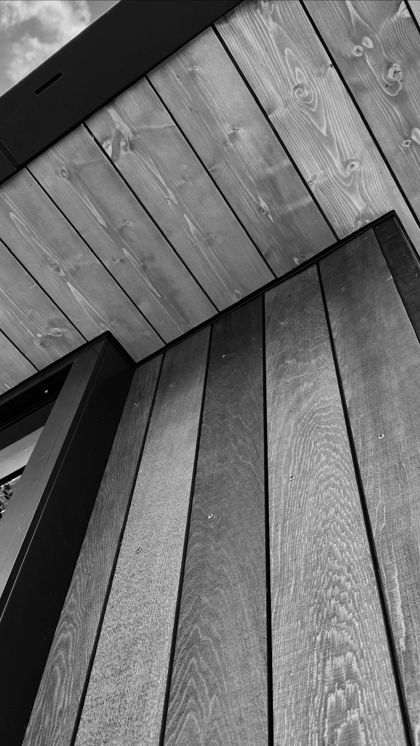 Black and white photo of wooden wall panels and ceiling with visible wood grain and knots.