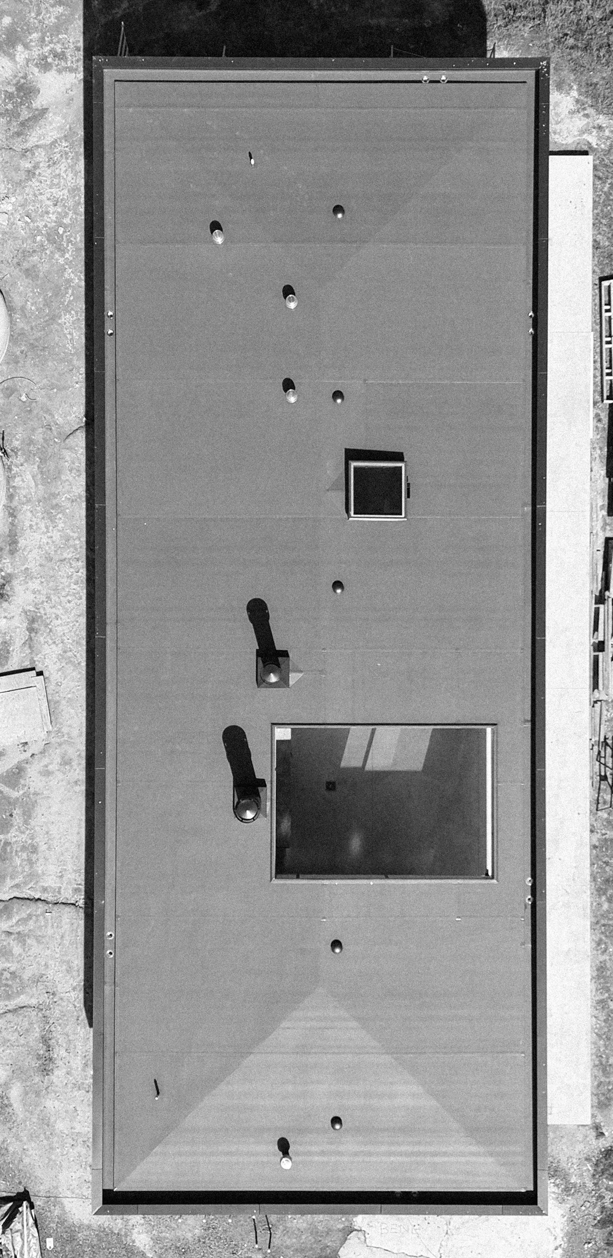 Black and white aerial view of an outdoor air-hockey table with two hockey sticks and four hockey pucks.