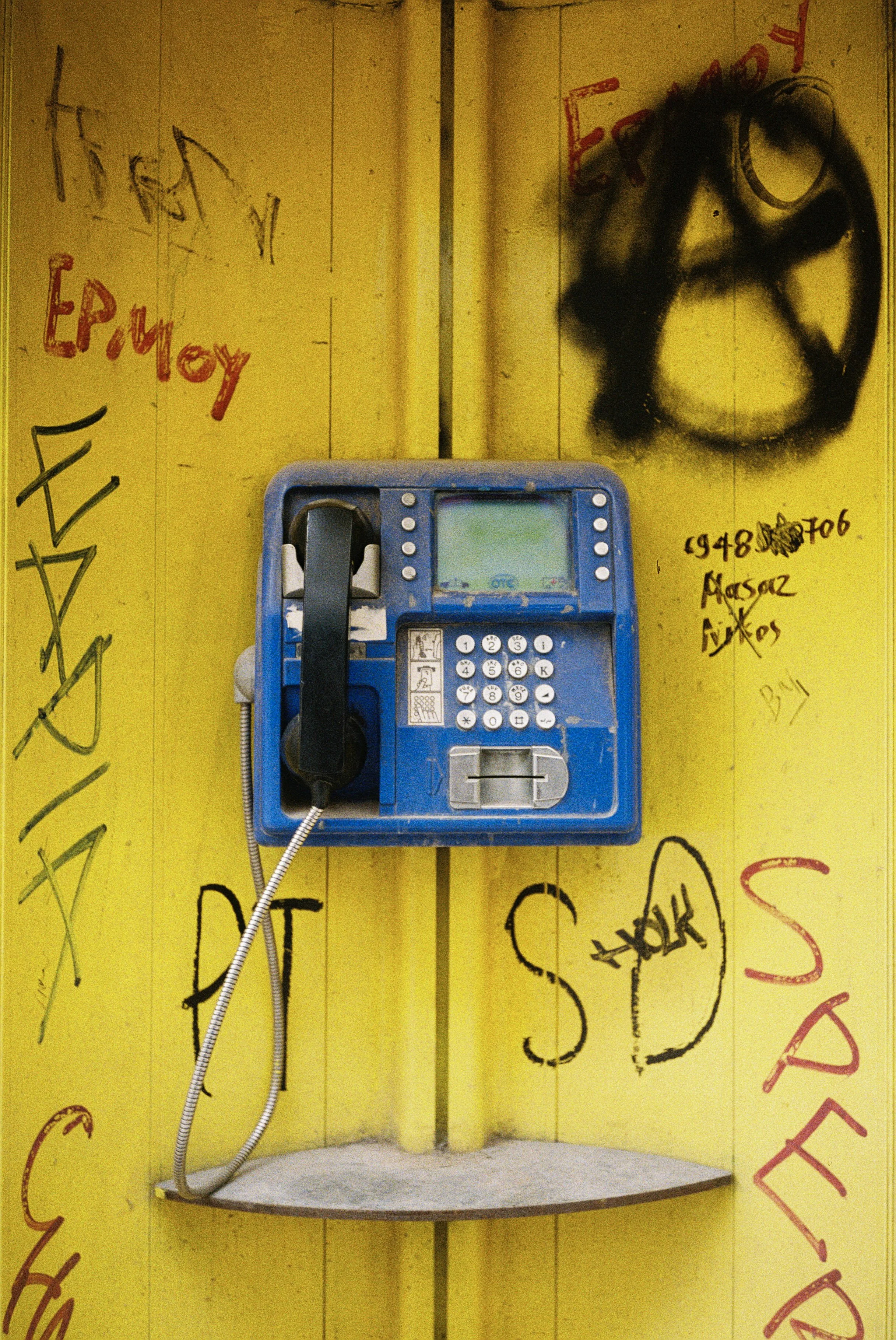 Ein öffentliches Telefon an einer gelben Wand mit Graffiti in deutscher Sprache.