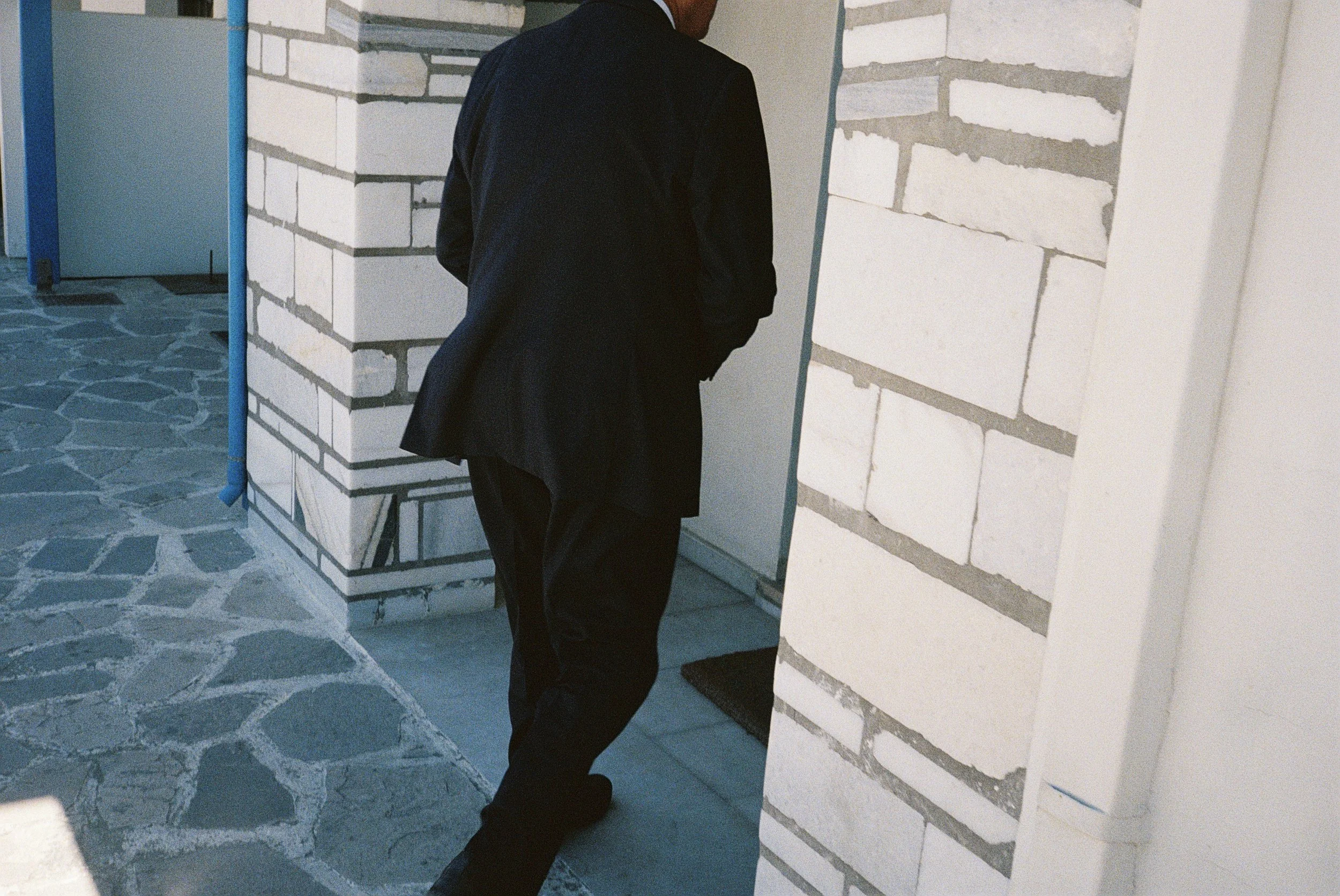 Eine Person in einem schwarzen Anzug schaut auf eine gemauerte Wand in einem Gebäude.