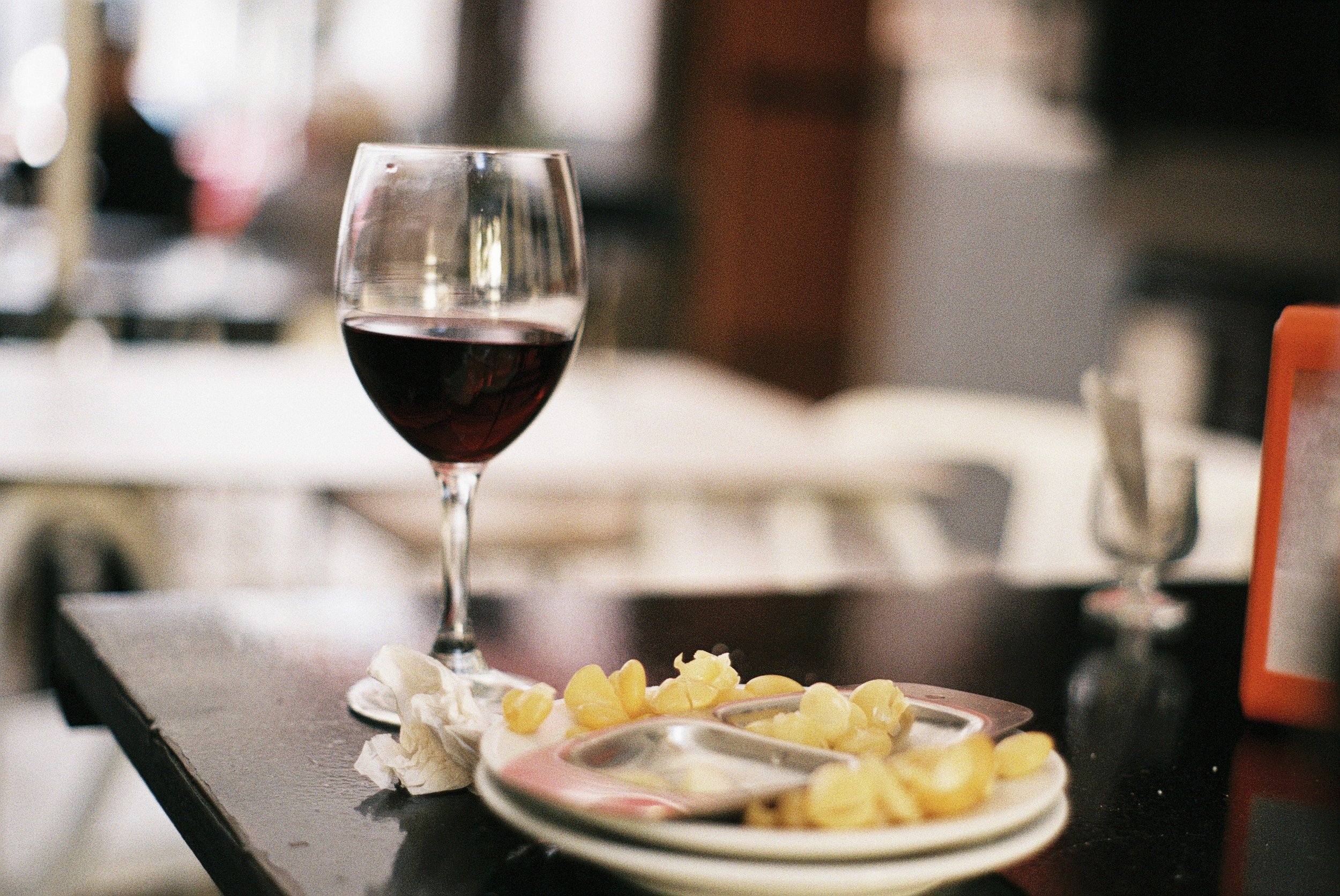 Ein Weinglas mit rotem Wein steht auf einem Tisch vor einem Teller mit Dessert, bestehend aus cremigem weißen Grund und gelben Früchten, daneben.