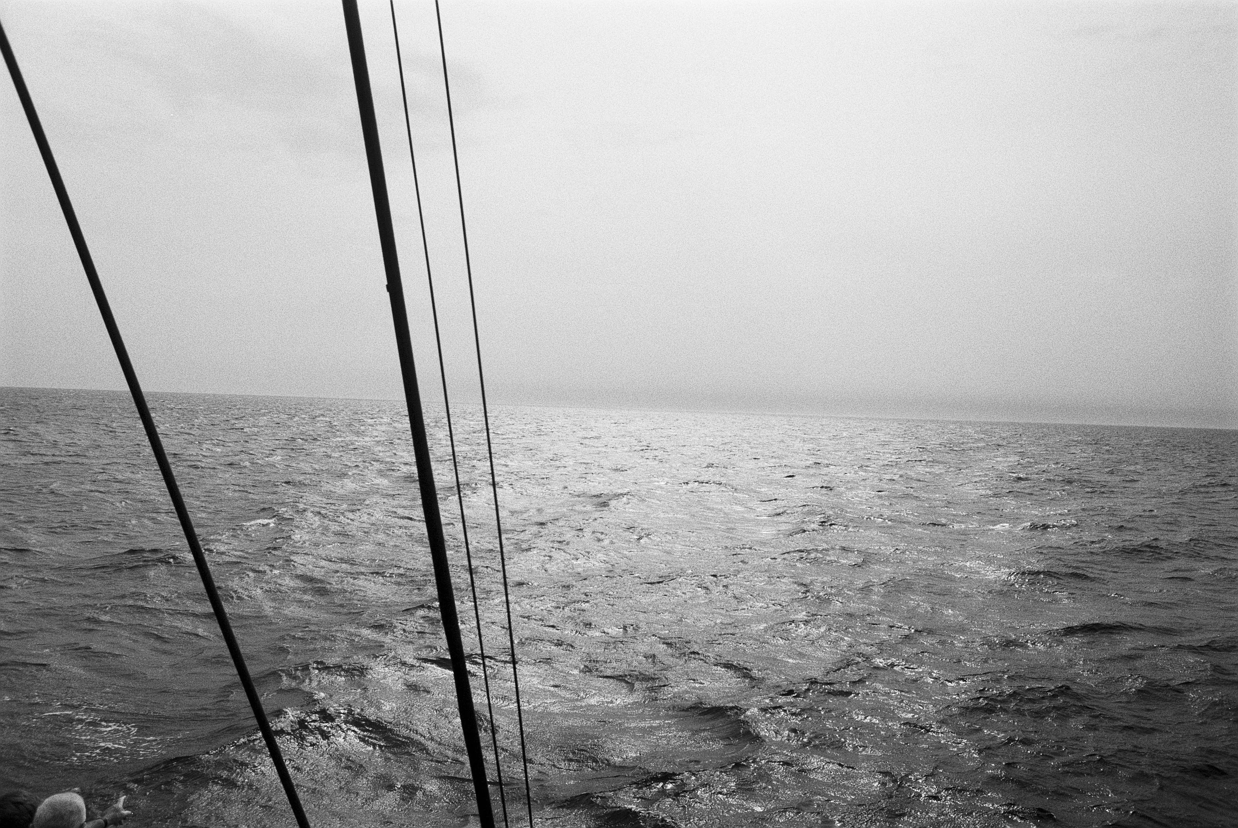 Blick vom Boot auf das Meer mit Wellen, Himmel und vier vertikale Seile im Vordergrund.