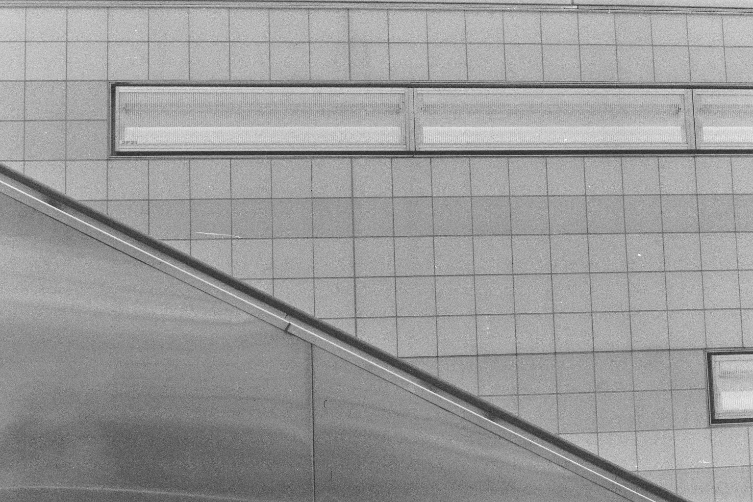 Ansicht eines modernen Gebäudes mit quadratischen Fliesen, zwei große Fenster und eine Edelstahlbrüstung.