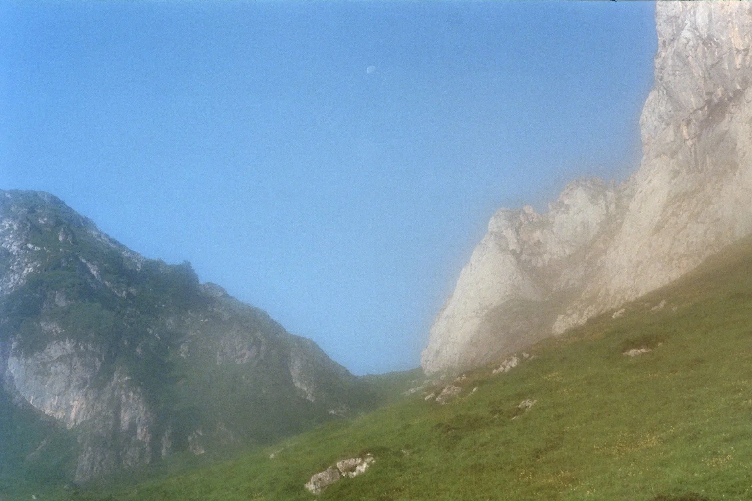 Berglandschaft mit grüner Wiese, steilen Felsen und klarem Himmel
