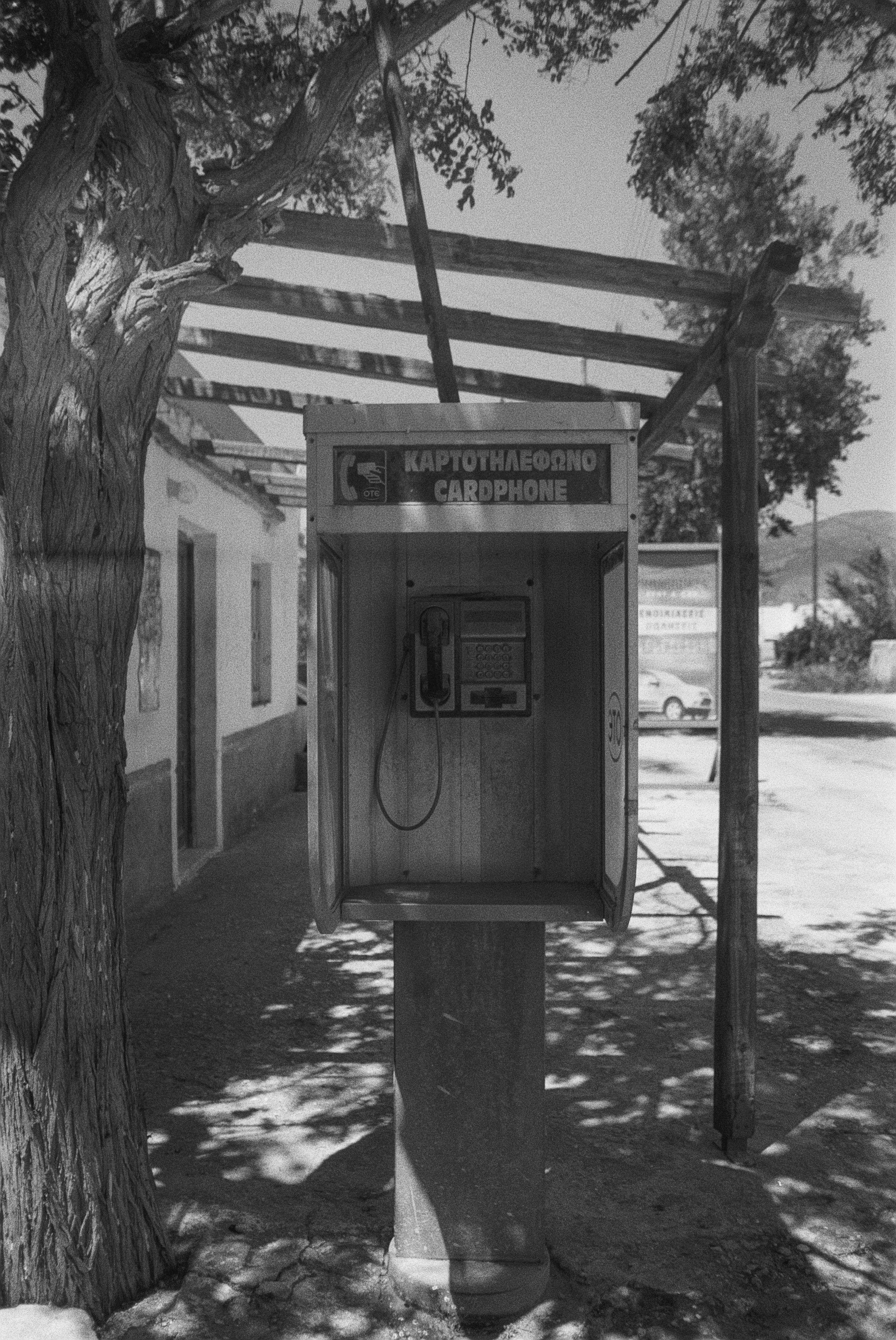 Ein alter Telefonautomat unter einem Baum, in schwarzer und weißer Aufnahme.