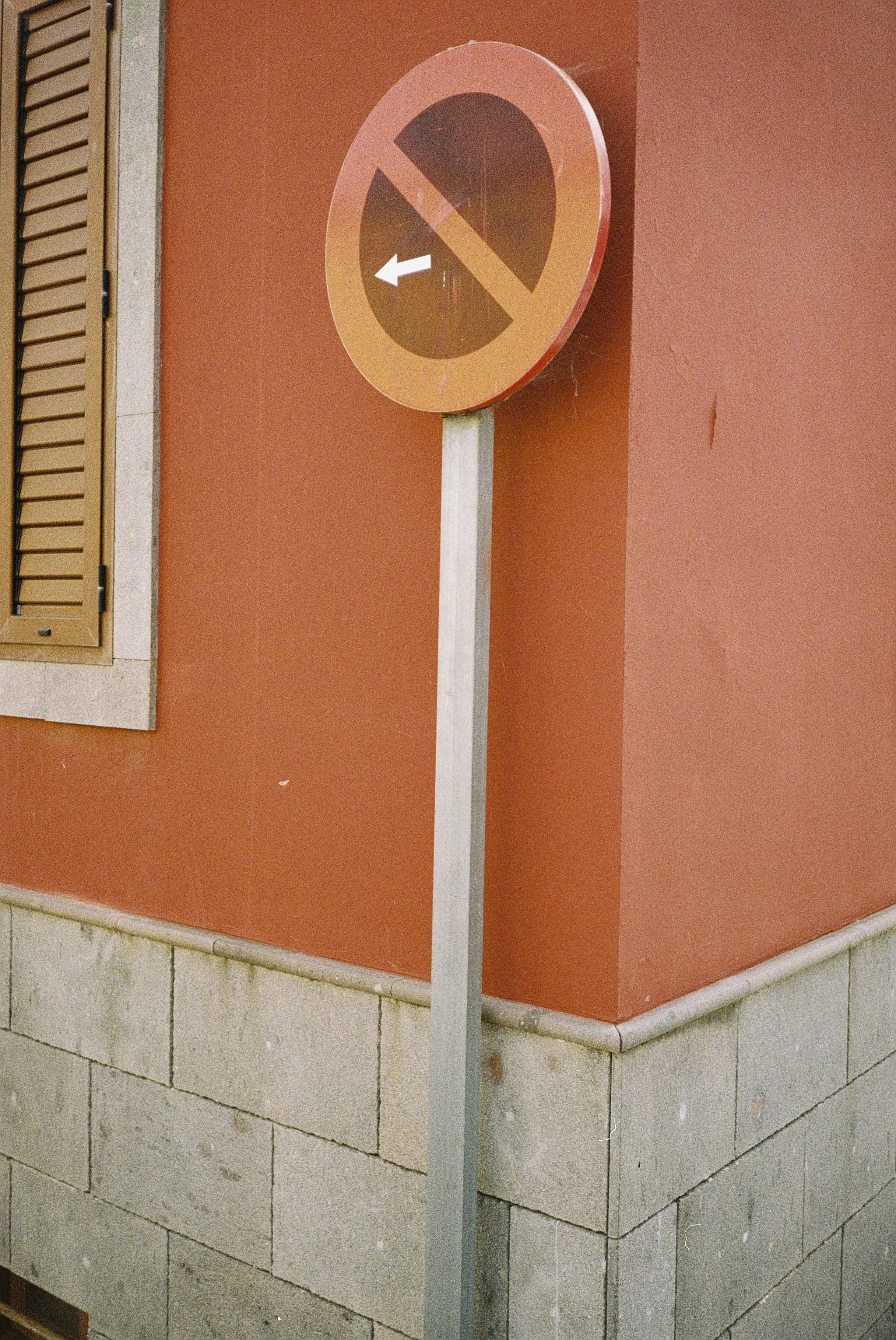 Standortschild mit einem durchgestrichenen Pfeil nach links an einer roten Hauswand.