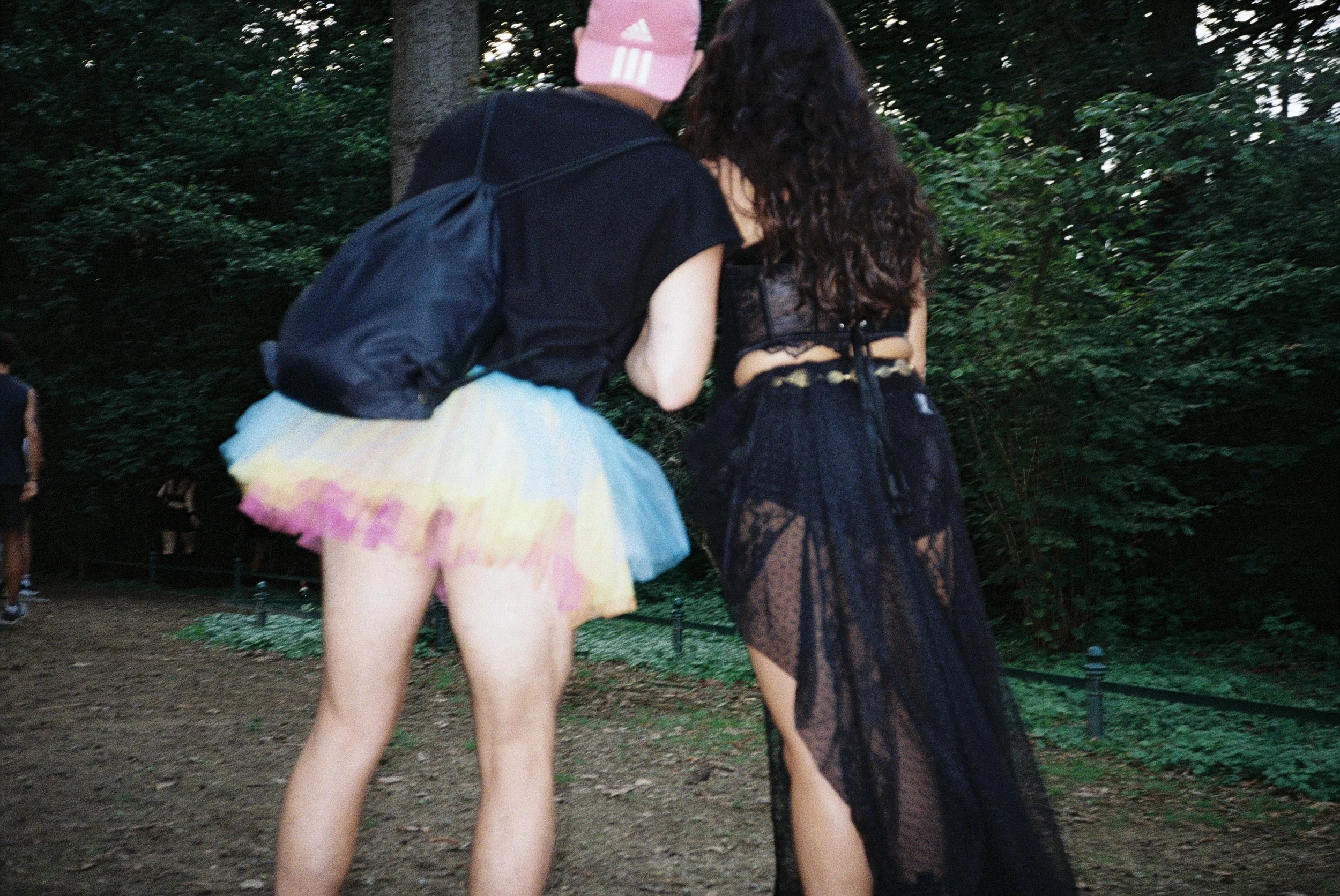 Zwei junge Frauen gehen im Park, eine trägt einen bunten Tüllrock und das andere ein schwarzes Spitzenkleid.